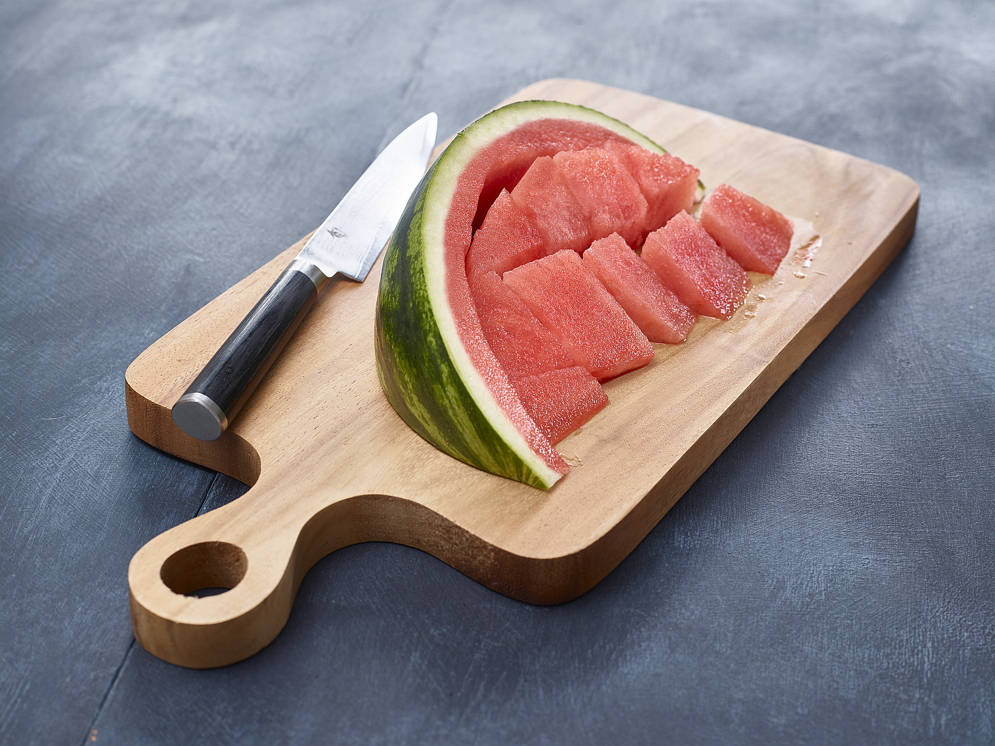 A cutting board with a watermelon being sliced into wedges on a bright kitchen counter