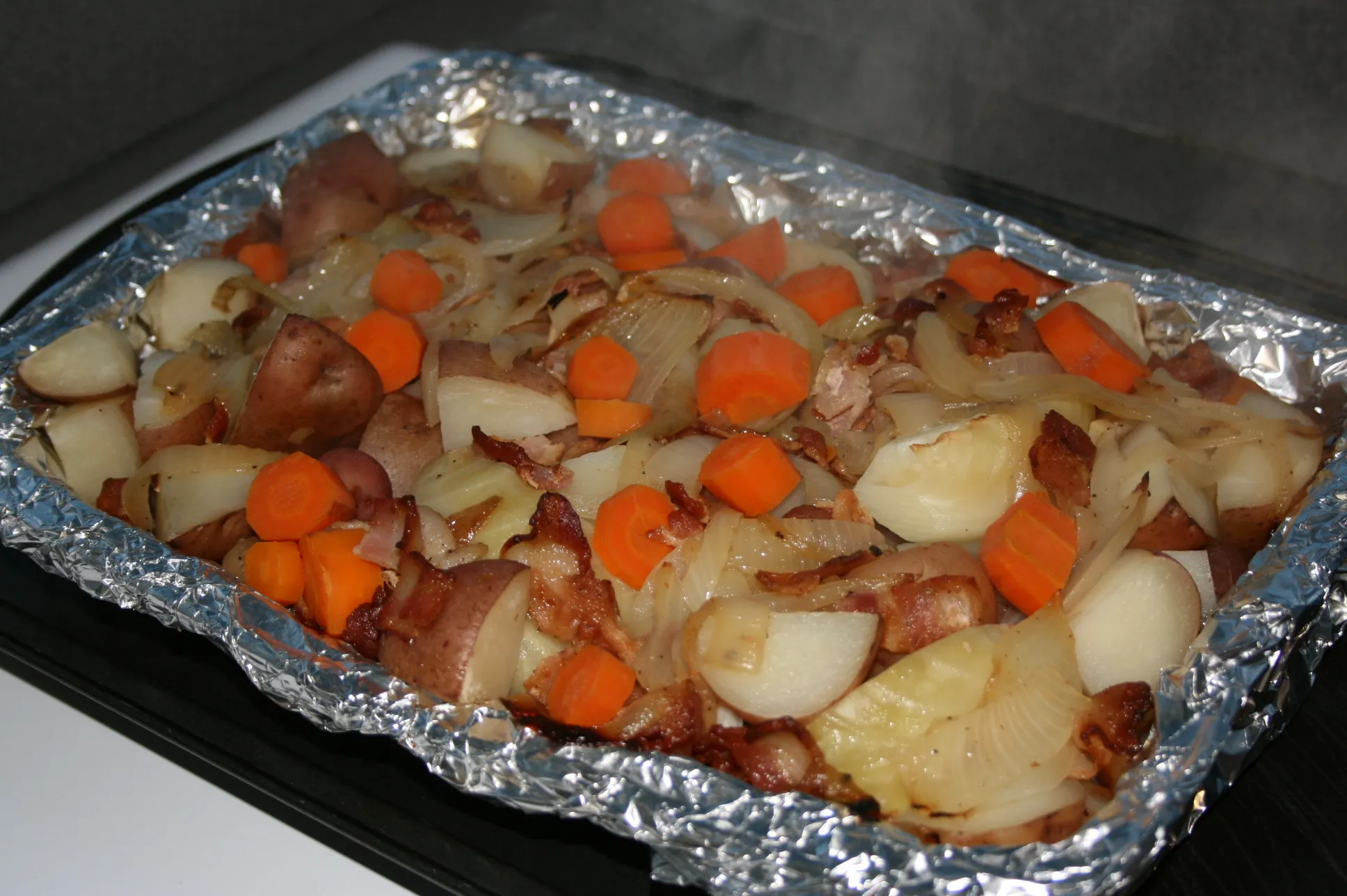 A cutting board with cabbage wedges, sliced carrots, and halved baby potatoes prepped and ready beside a slow cooker insert