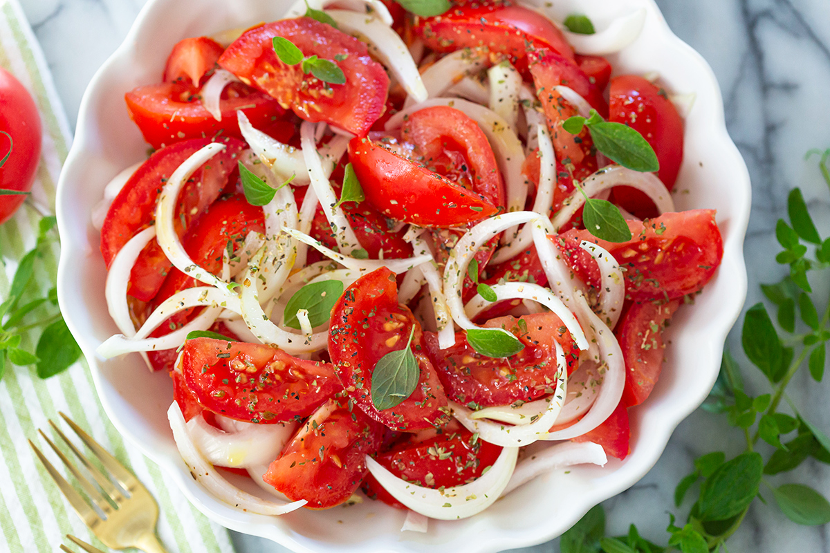 A cutting board with finely chopped white onion and sliced roma tomato wedges next to a knife on a kitchen counter