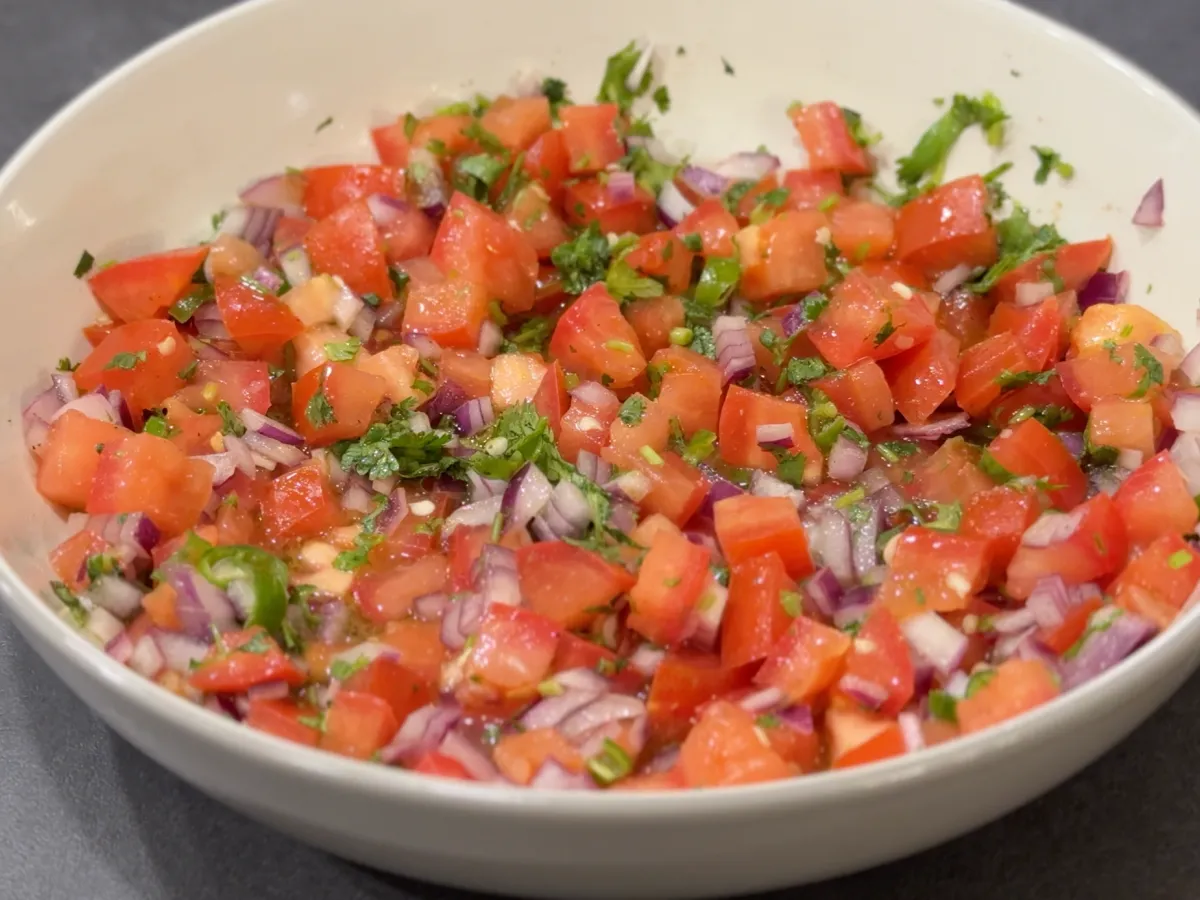 A cutting board with neatly diced red onion and chopped cilantro beside a chef’s knife on a kitchen counter in warm natural light