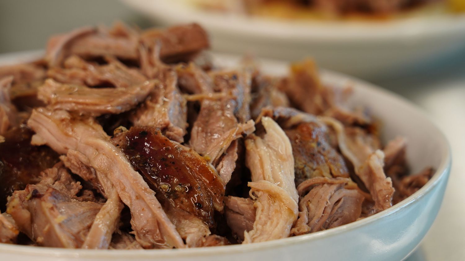 A deep baking dish holding a roasted Boston butt with dark caramelized bark, surrounded by rendered juices on a warm kitchen counter under soft natural light