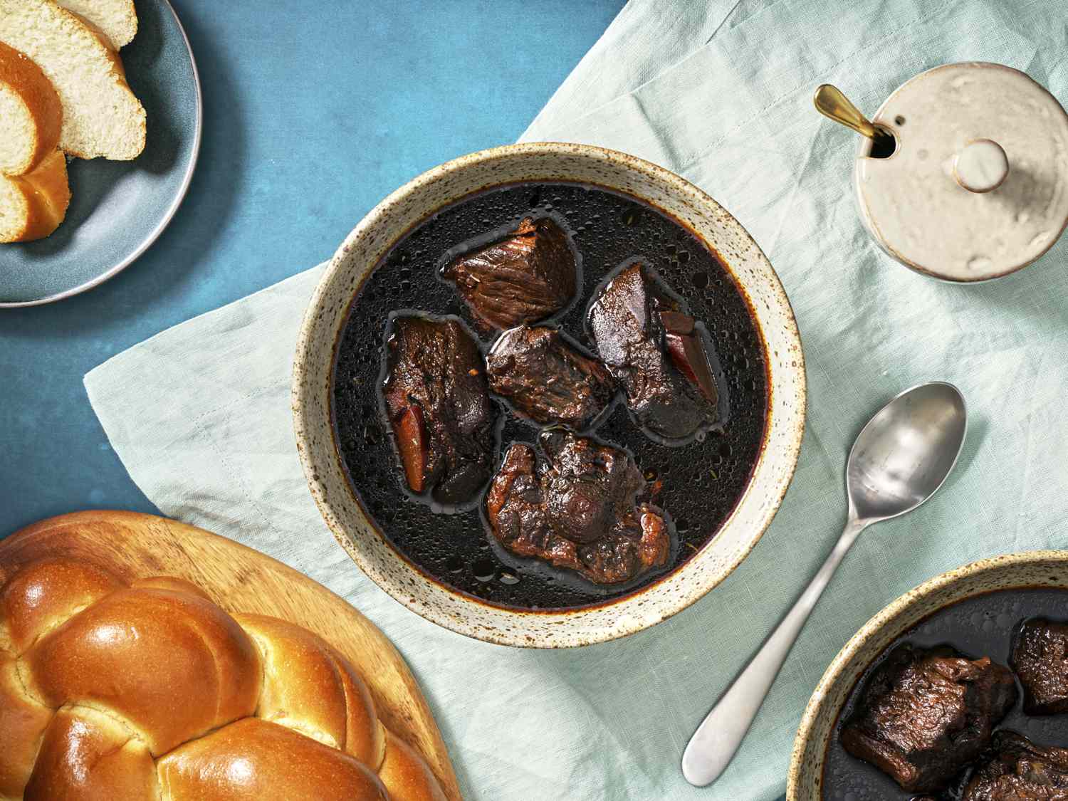 A deep bowl of glossy Guyanese pepperpot with tender chunks of beef in a dark cassareep gravy, served with warm bread