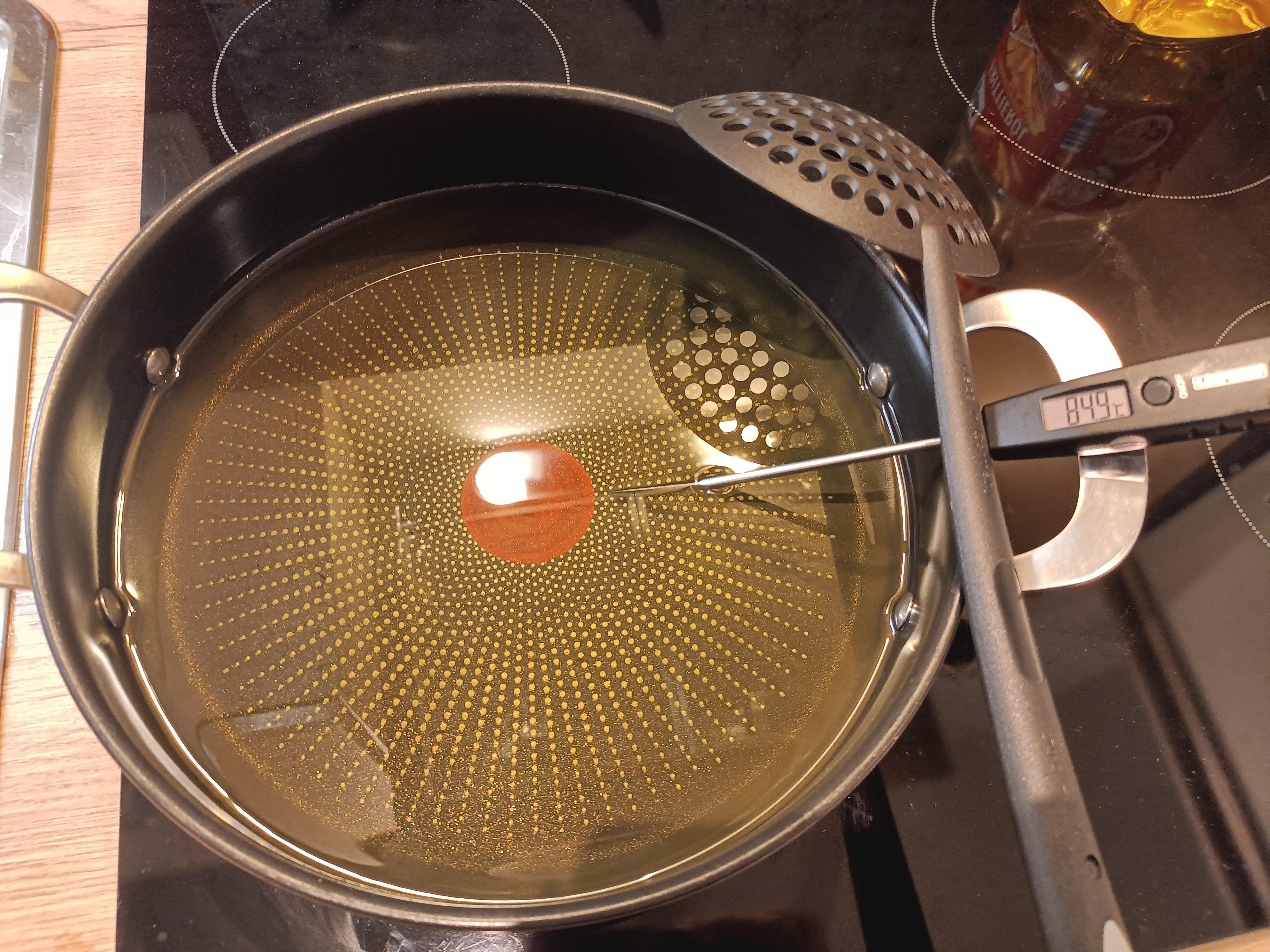A deep cast iron skillet on a stovetop with oil heating and a thermometer clipped to the side, ready for frying bread