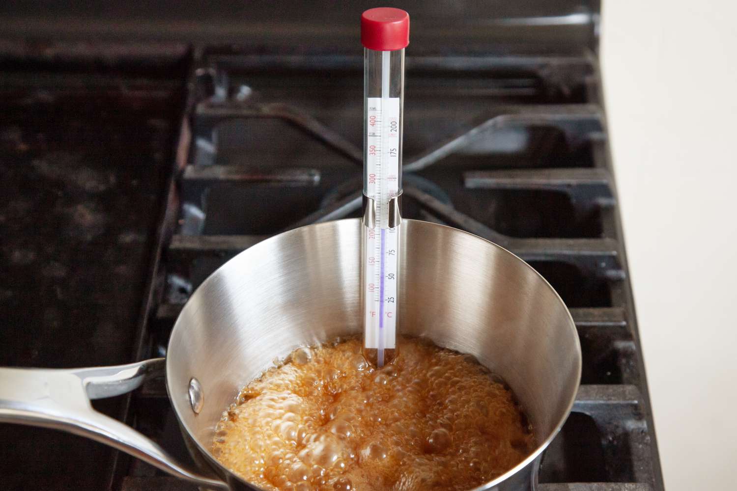 A deep-fry thermometer clipped to a pot showing hot oil at frying temperature on a stovetop