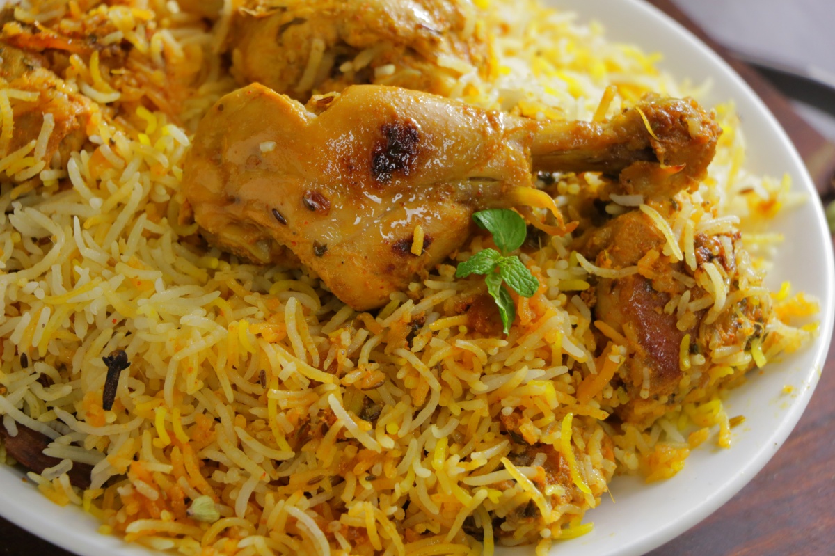 A deep serving platter of Hyderabadi chicken dum biryani with long basmati rice grains, visible fried onions, fresh mint, and a saffron-tinted top layer on a wooden table