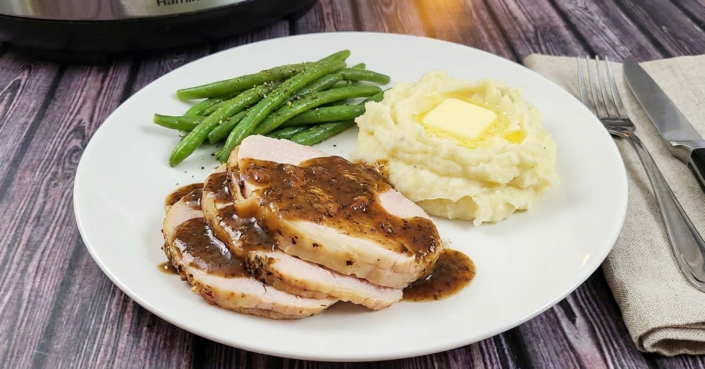 A dinner plate with sliced turkey breast topped with gravy, served alongside mashed potatoes and green beans on a simple table setting