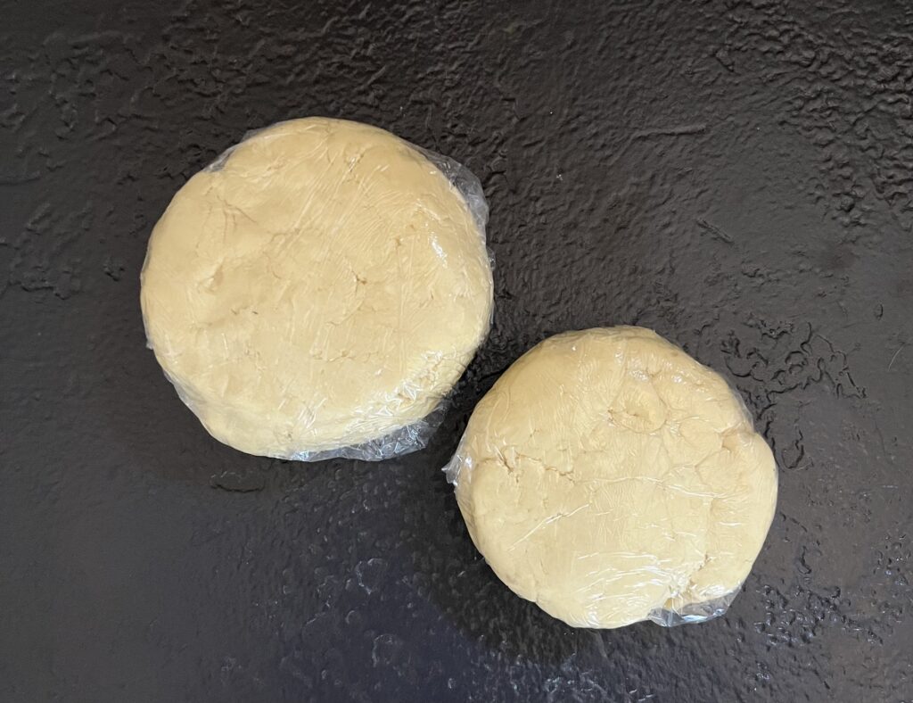 A disk of Christmas biscuit dough wrapped in plastic wrap resting on a cutting board in a home kitchen
