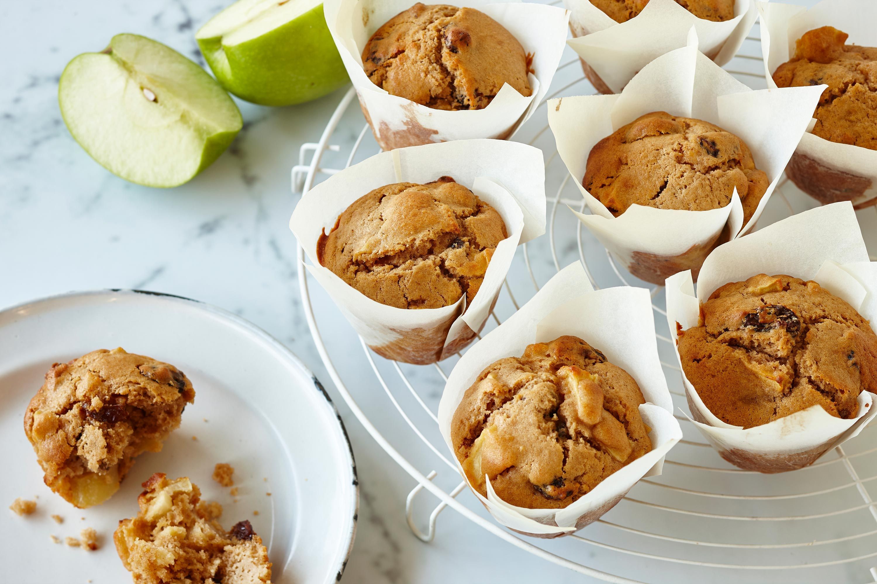 A dozen cinnamon apple muffins with golden domed tops cooling on a wire rack on a bright kitchen counter