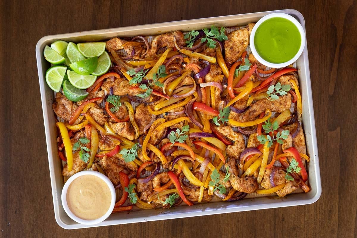 A family-style dinner table with a platter of chicken fajitas, bowls of toppings like shredded cheese and salsa, and a stack of warm tortillas ready for serving