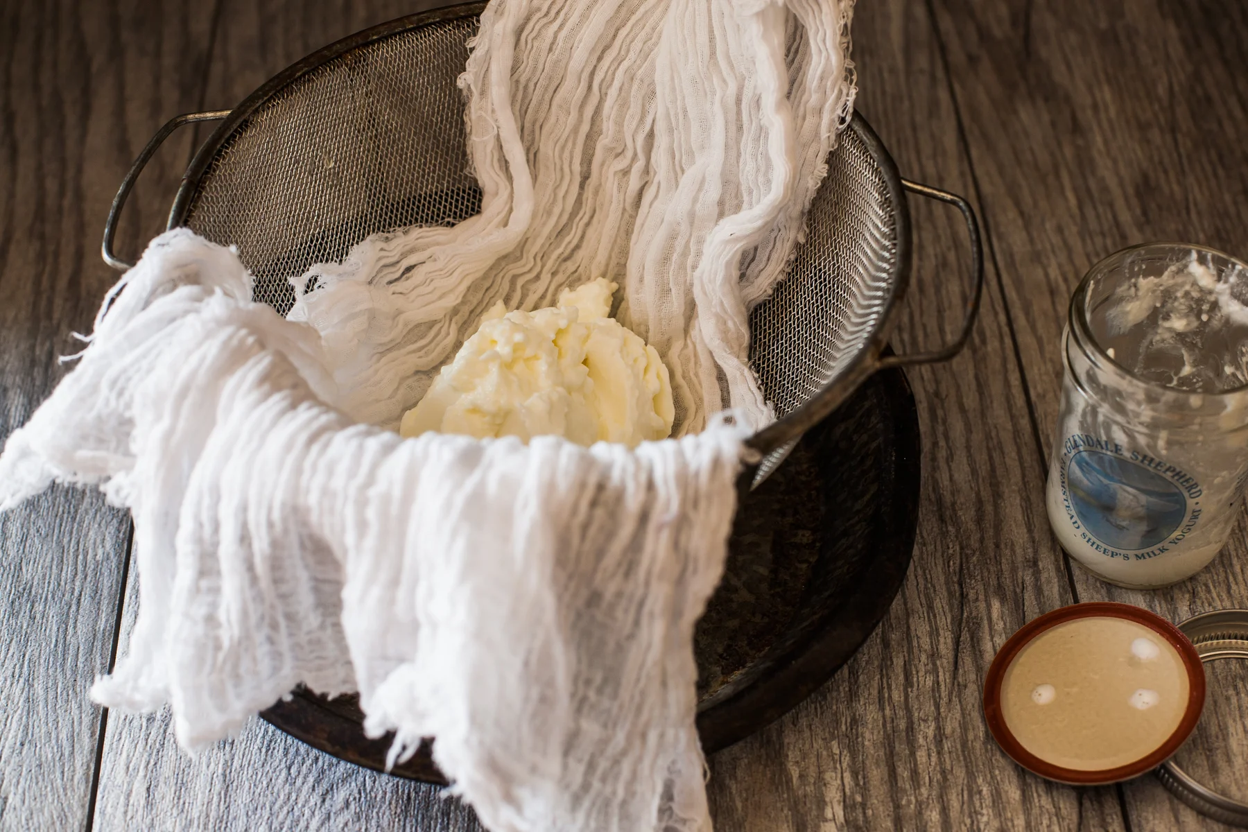 A fine mesh strainer lined with cheesecloth holding salted yogurt as it strains over a bowl on a kitchen counter