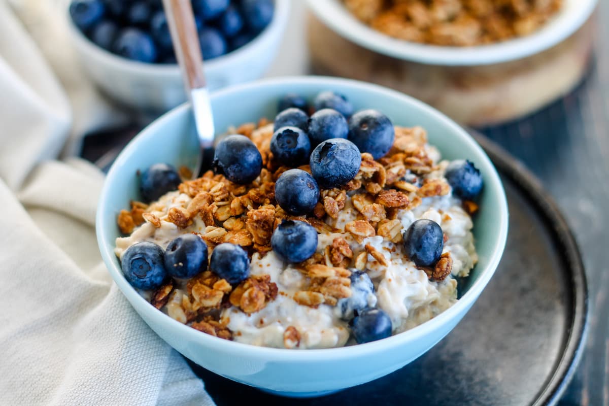 A finished jar of overnight oats topped with fresh berries and a light sprinkle of cinnamon, sitting on a breakfast table with a spoon
