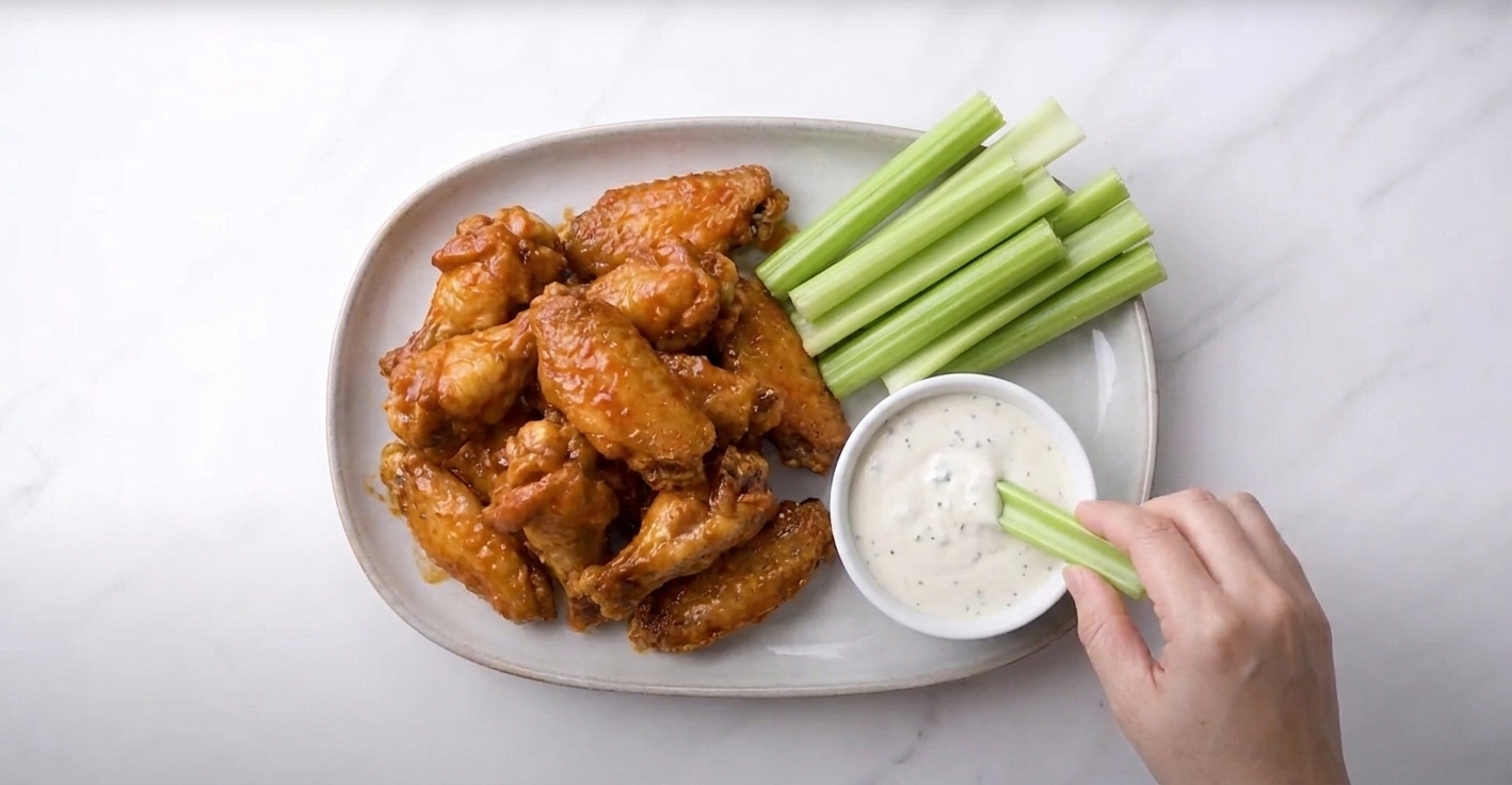 A finished platter of Buffalo wings served with celery sticks and a bowl of blue cheese dressing