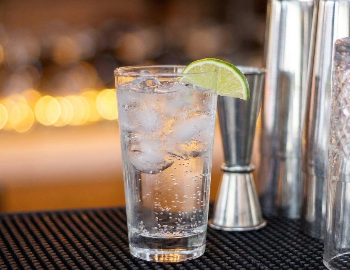 A finished vodka soda in a highball glass with lime wedge garnish on a simple table setting