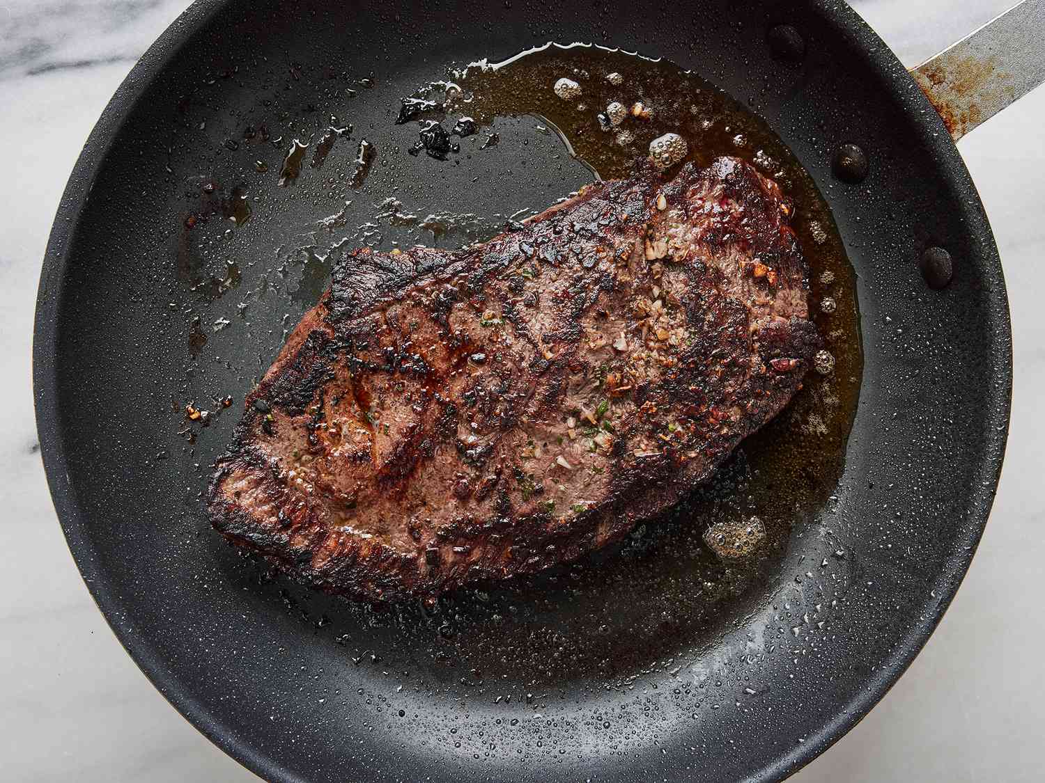 A flat iron steak sizzling in a hot cast iron skillet with browned edges forming, seen from overhead on a stovetop