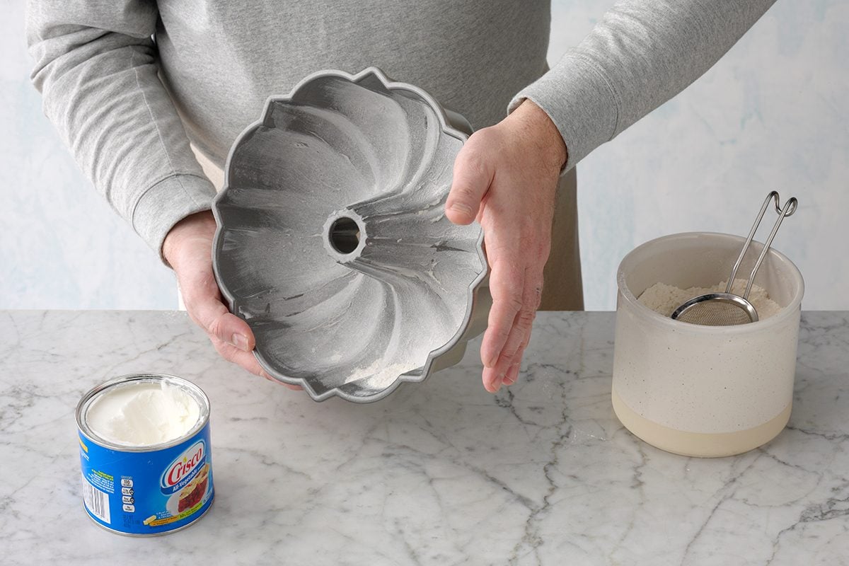 A floured bundt pan sitting on a kitchen counter with a light dusting of flour visible in the grooves