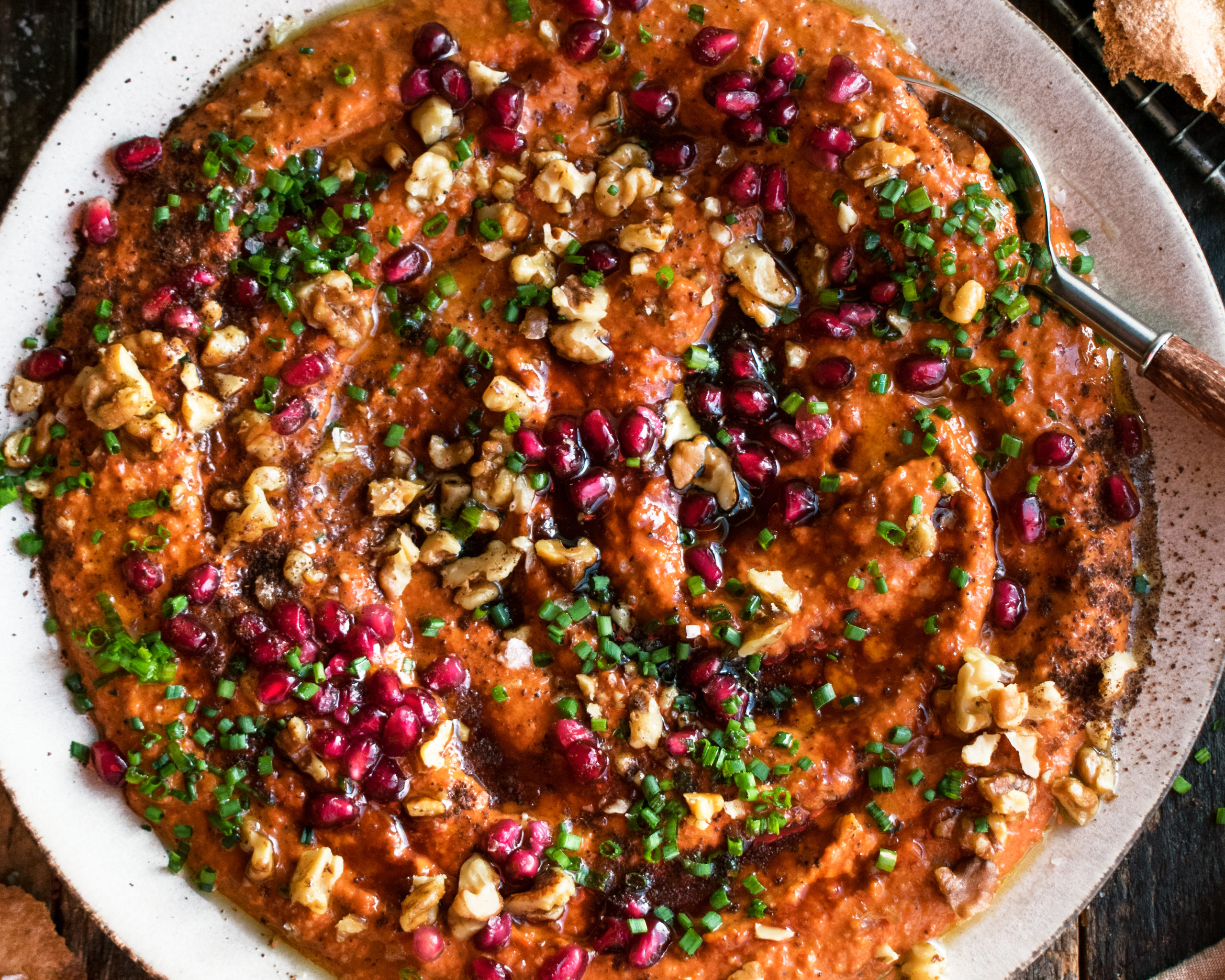 A food processor mid-blend with a creamy orange-red roasted pepper dip swirling inside on a bright kitchen counter