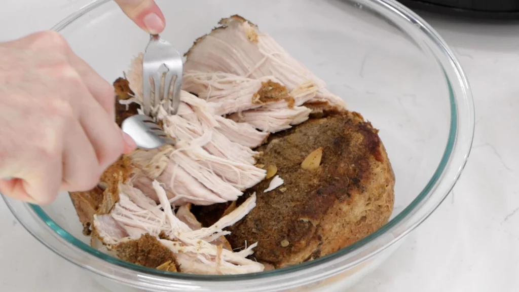 A fork pulls tender strands from a slow-cooked pork roast on a cutting board