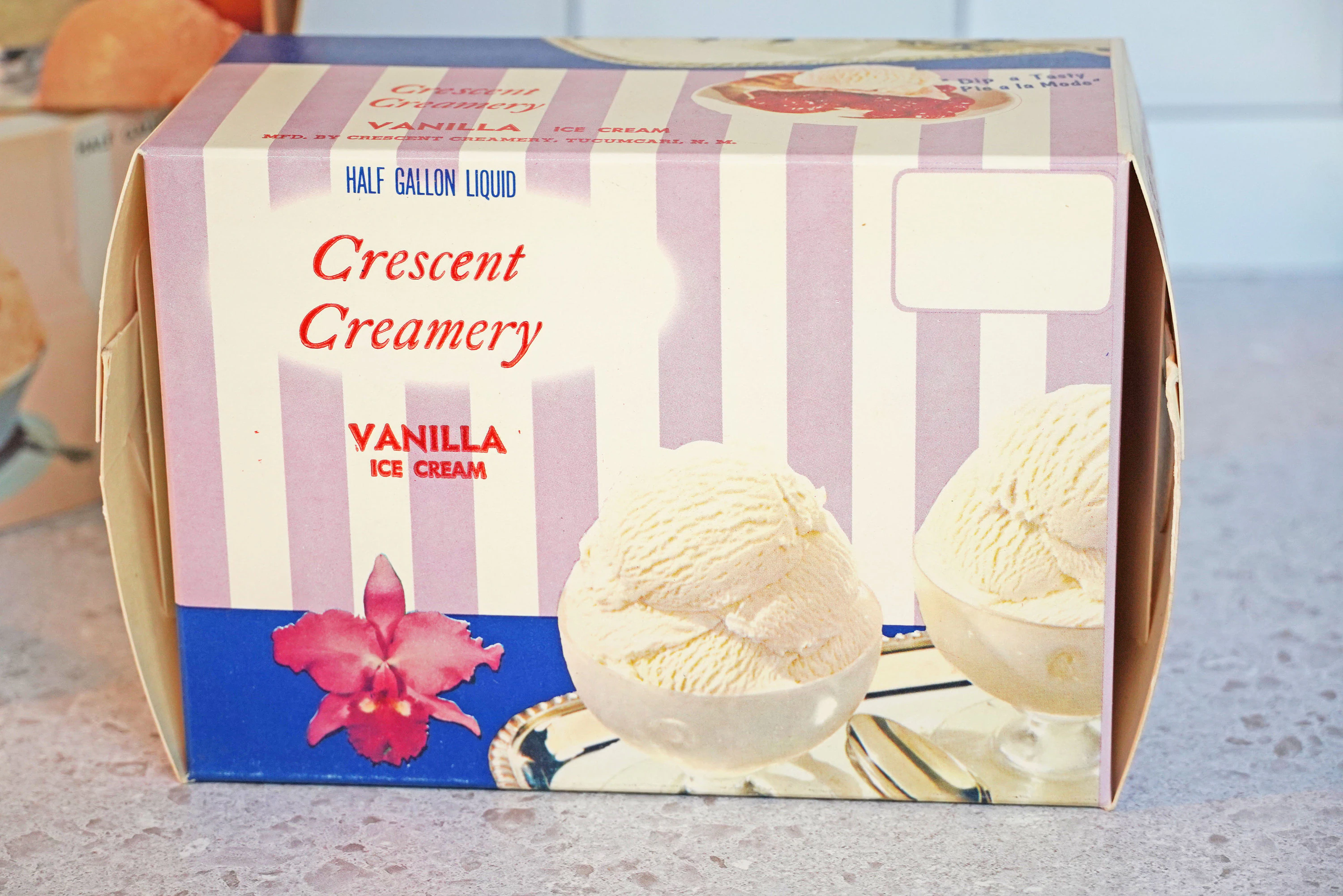 A freezer-safe container filled with vanilla ice cream, parchment pressed on top, sitting on a kitchen counter next to a lid