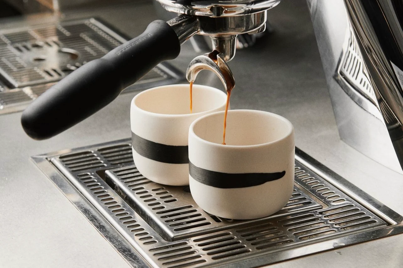 A fresh espresso shot being poured into a wide ceramic mug on a kitchen counter