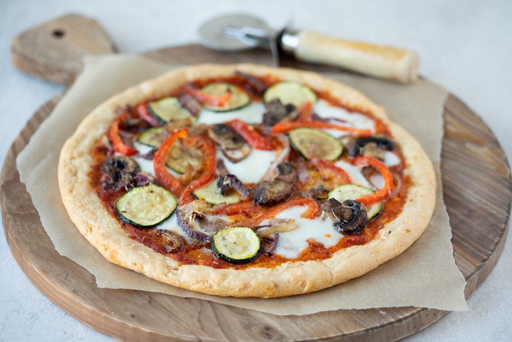 A freshly baked gluten-free pizza base on parchment paper with golden crisp edges and a lightly blistered surface on a sheet pan