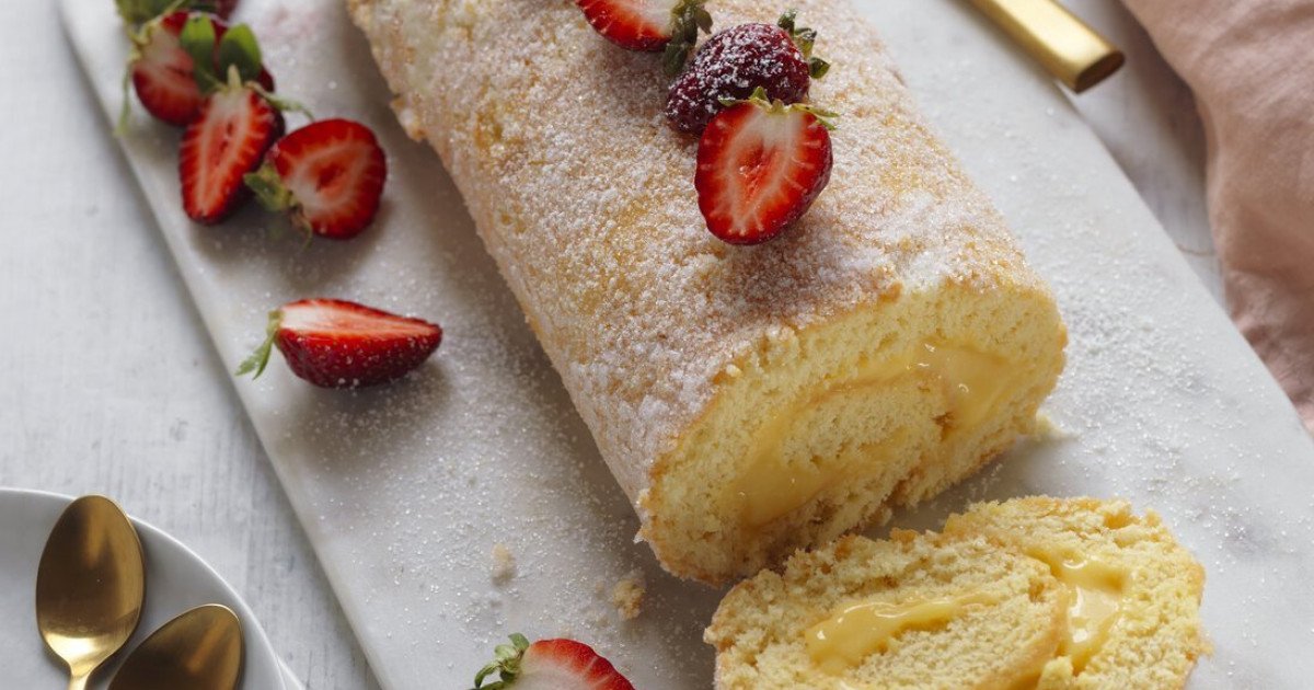 A freshly baked golden Swiss roll sponge cake in a jelly roll pan lined with parchment paper on a neutral kitchen counter