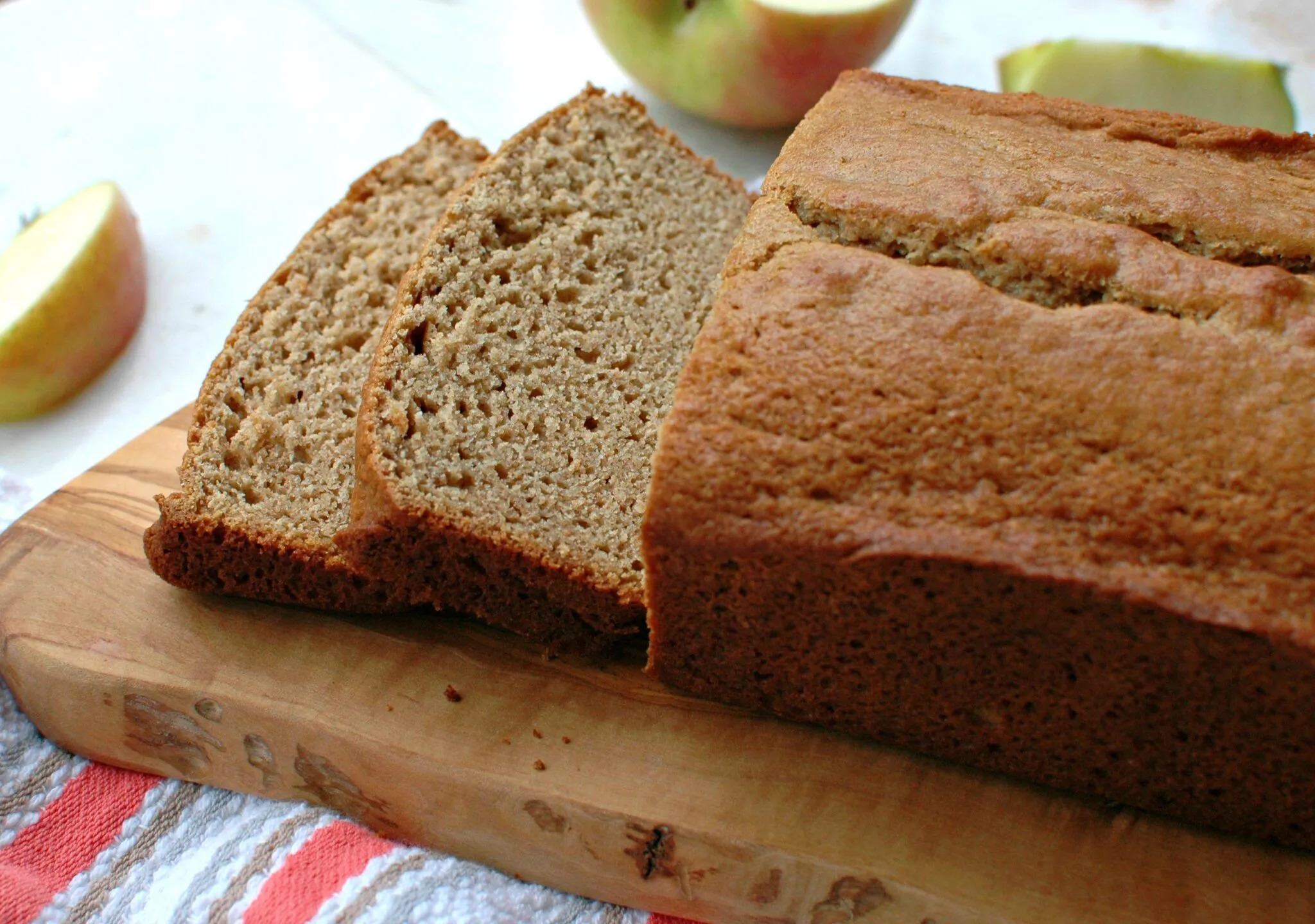 A freshly baked loaf of applesauce bread sliced on a wooden cutting board with a few crumbs scattered, warm natural kitchen light