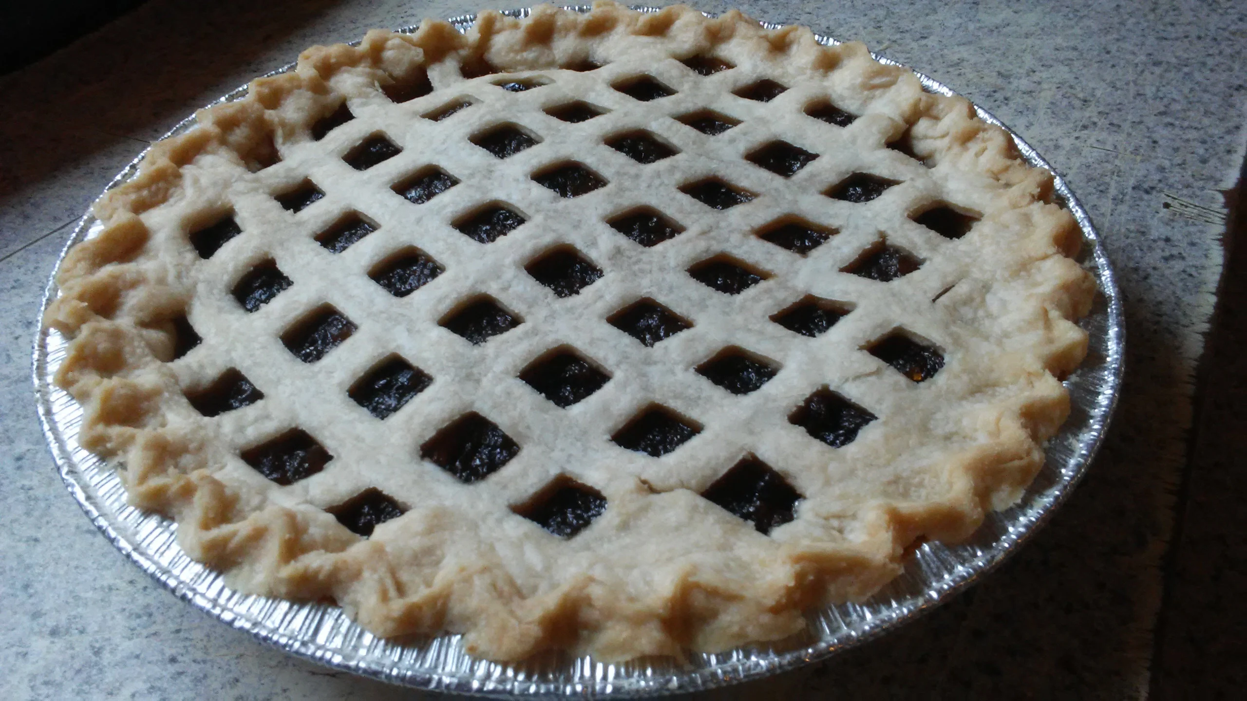 A freshly baked mincemeat pie with a golden lattice crust cooling on a wire rack on a warm wood countertop