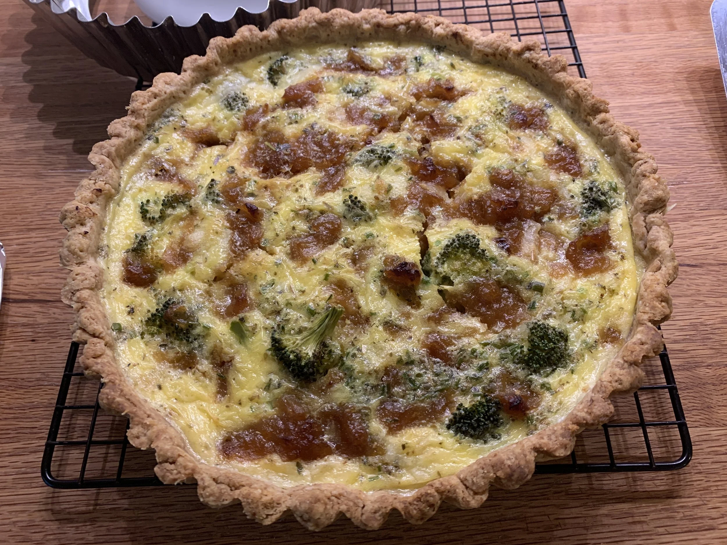 A freshly baked quiche in a ceramic pie dish cooling on a wire rack on a kitchen counter