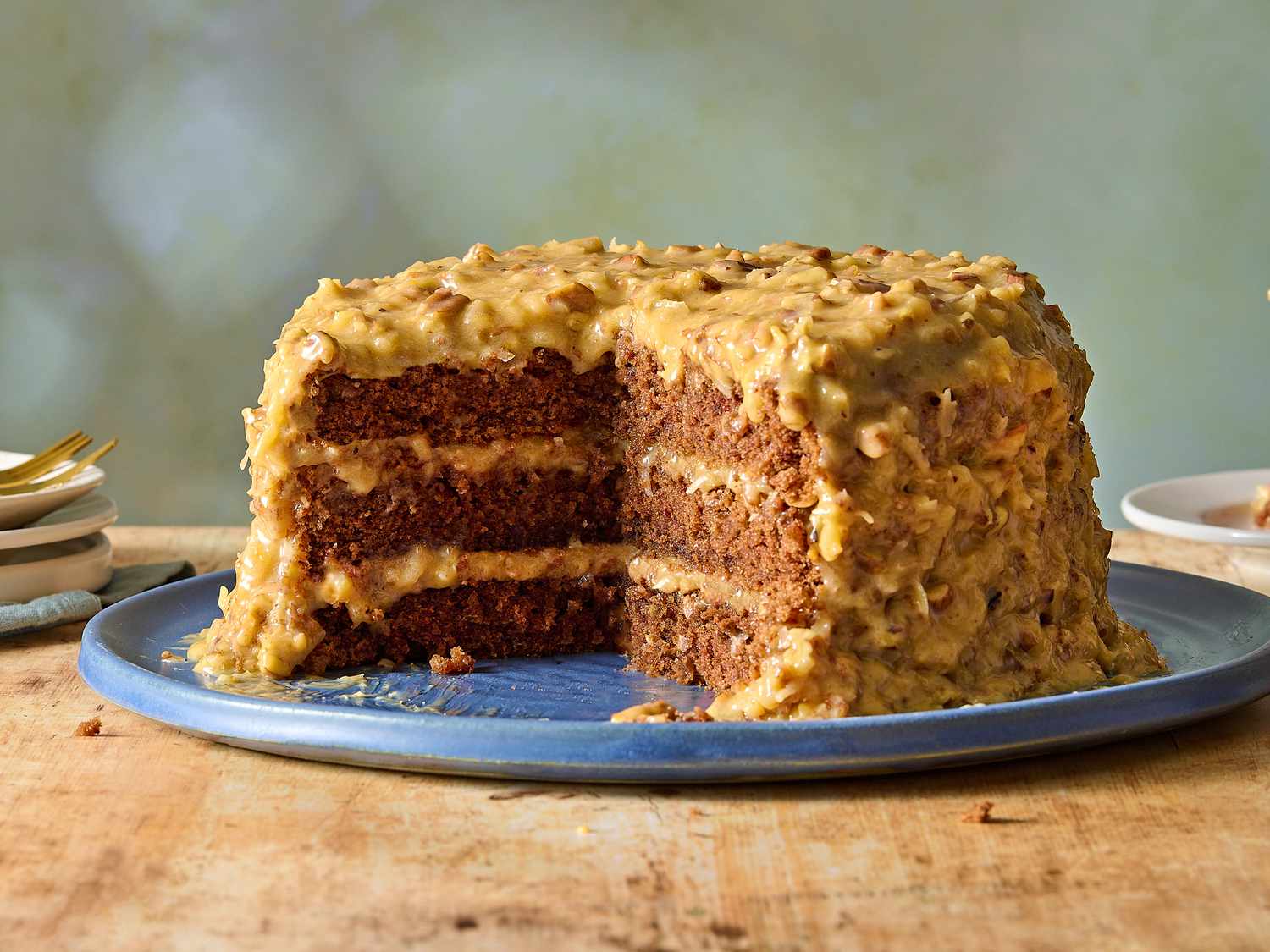 A freshly frosted German chocolate cake with thick coconut pecan icing piled between layers and spread on top, on a clean kitchen counter with warm natural light