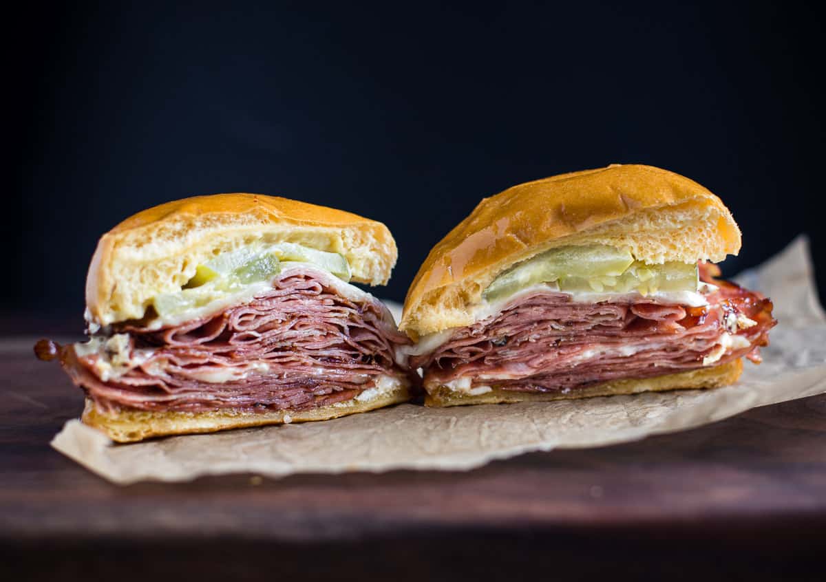 A freshly made crispy mortadella sandwich with melty provolone spilling over the edges on a toasted kaiser roll, set on a wooden cutting board with a small dish of mustard in a warm home kitchen