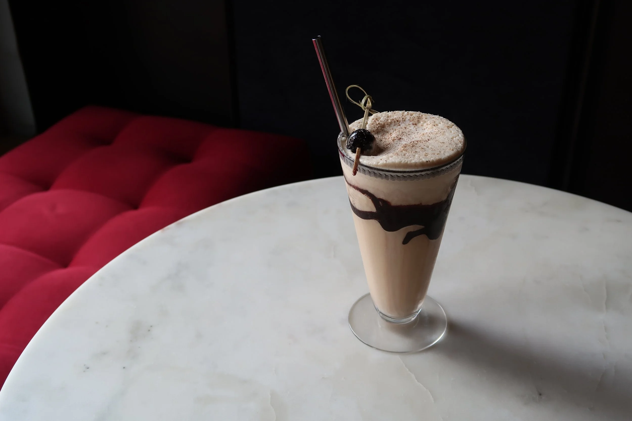 A frosty Bushwacker cocktail in a tall glass with chocolate syrup drizzled inside the glass, topped with whipped cream and chocolate shavings on a bright kitchen counter
