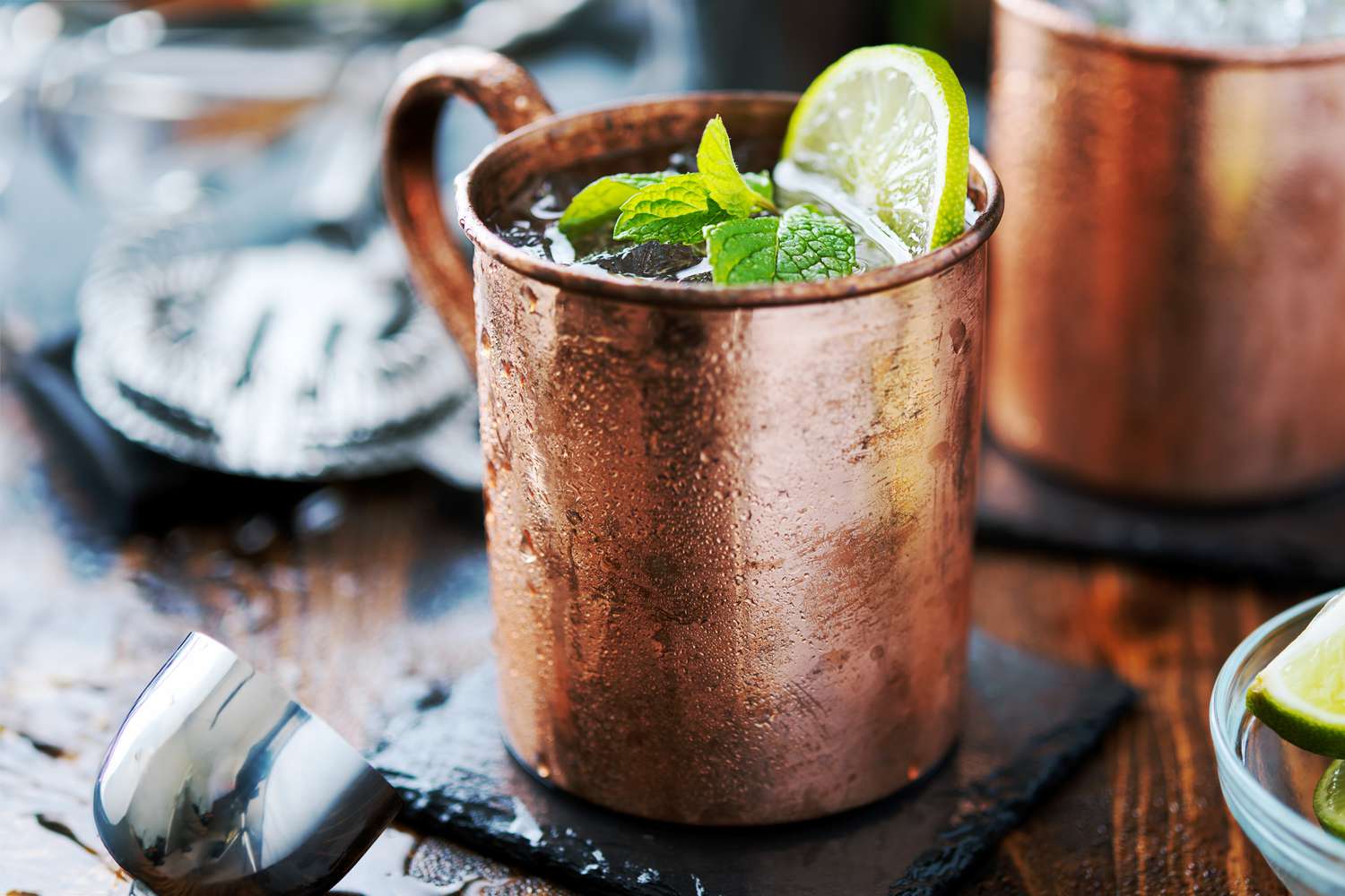 A frosty copper mug filled with a Kentucky Mule cocktail, crushed ice, lime wedge, and fresh mint on a warm wood kitchen counter with soft natural light