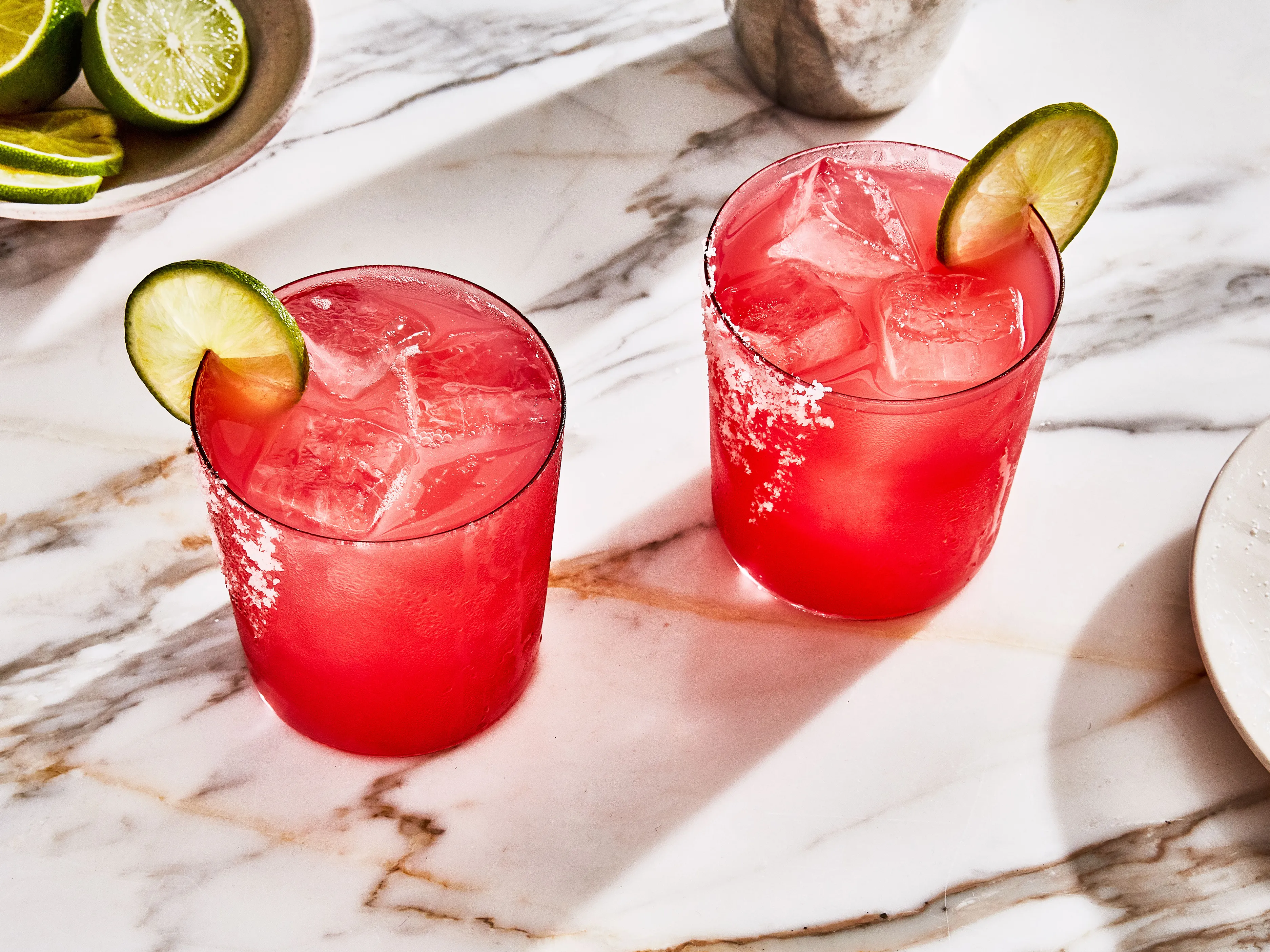 A frosty watermelon margarita in a rocks glass with a lime wedge and a salt rim on a light kitchen counter in natural window light