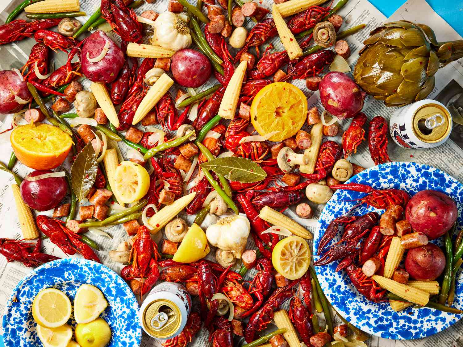 A full crawfish boil spread on a paper-covered table with red crawfish, corn on the cob, halved potatoes, sliced sausage, and lemon halves under warm kitchen lighting