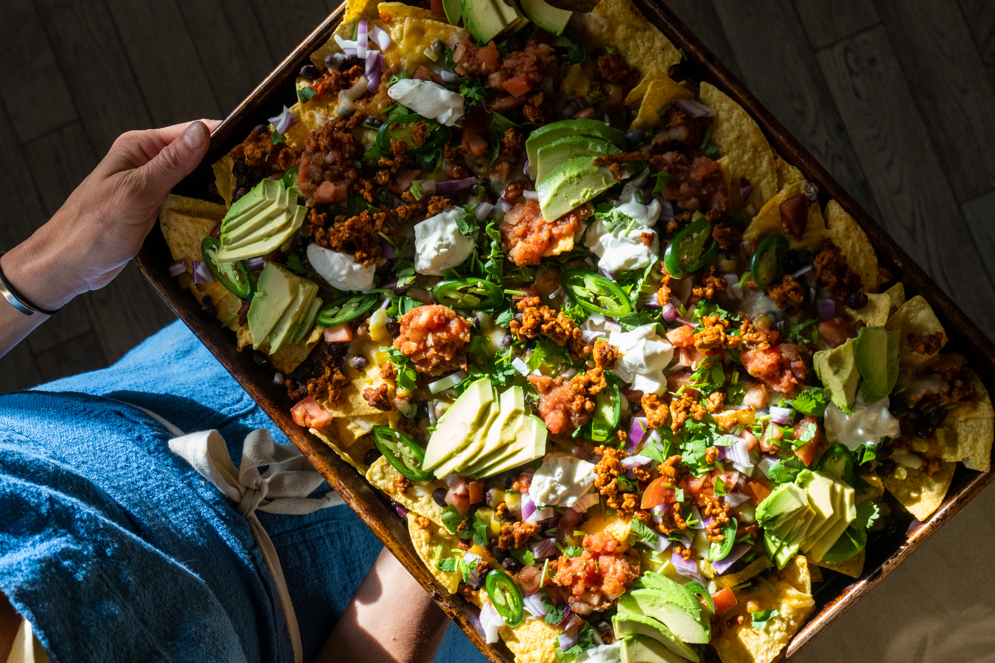 A full sheet pan of chicken nachos with melted cheese, black beans, jalapeños, diced tomatoes, and cilantro on a kitchen counter