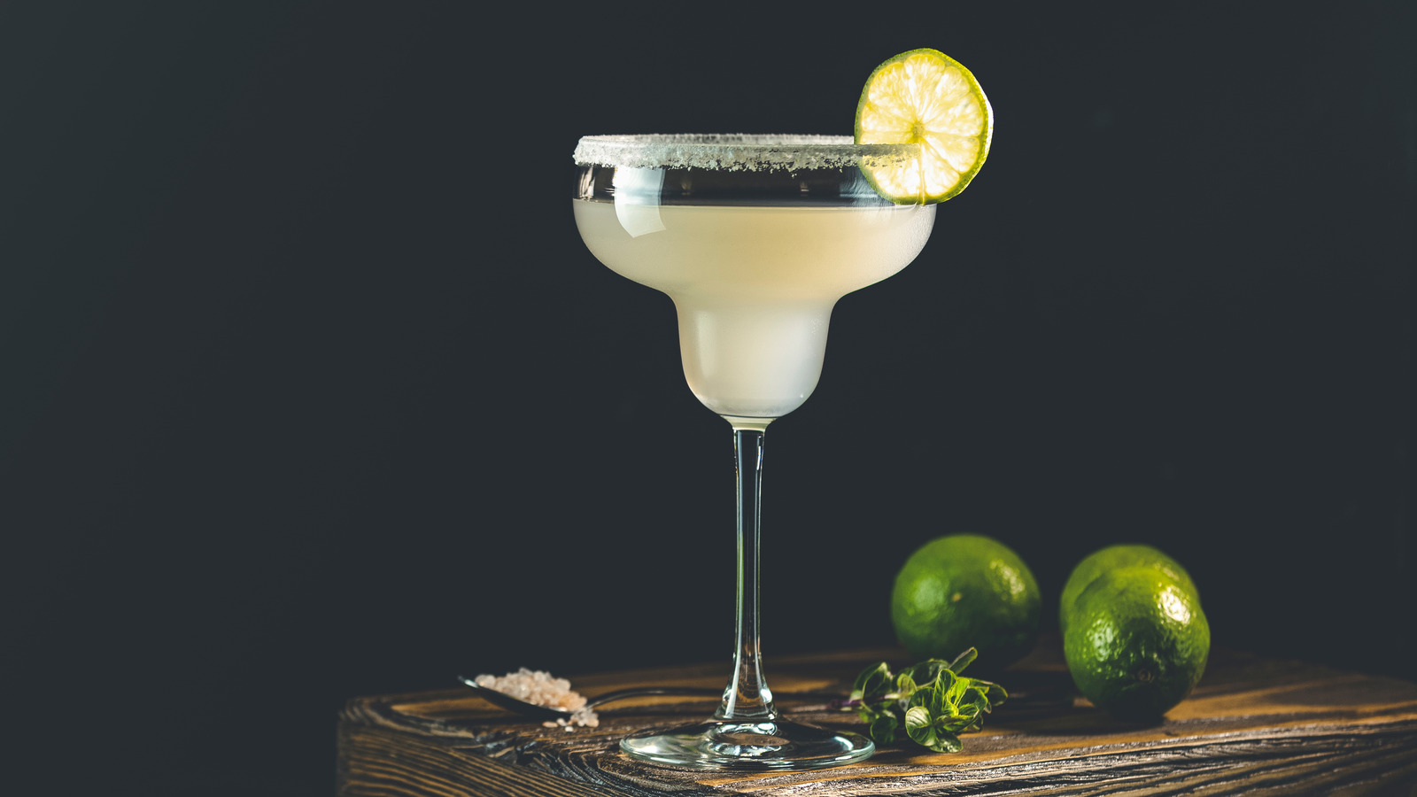 A glass being rimmed with a lime wedge beside a small plate of kosher salt on a kitchen counter