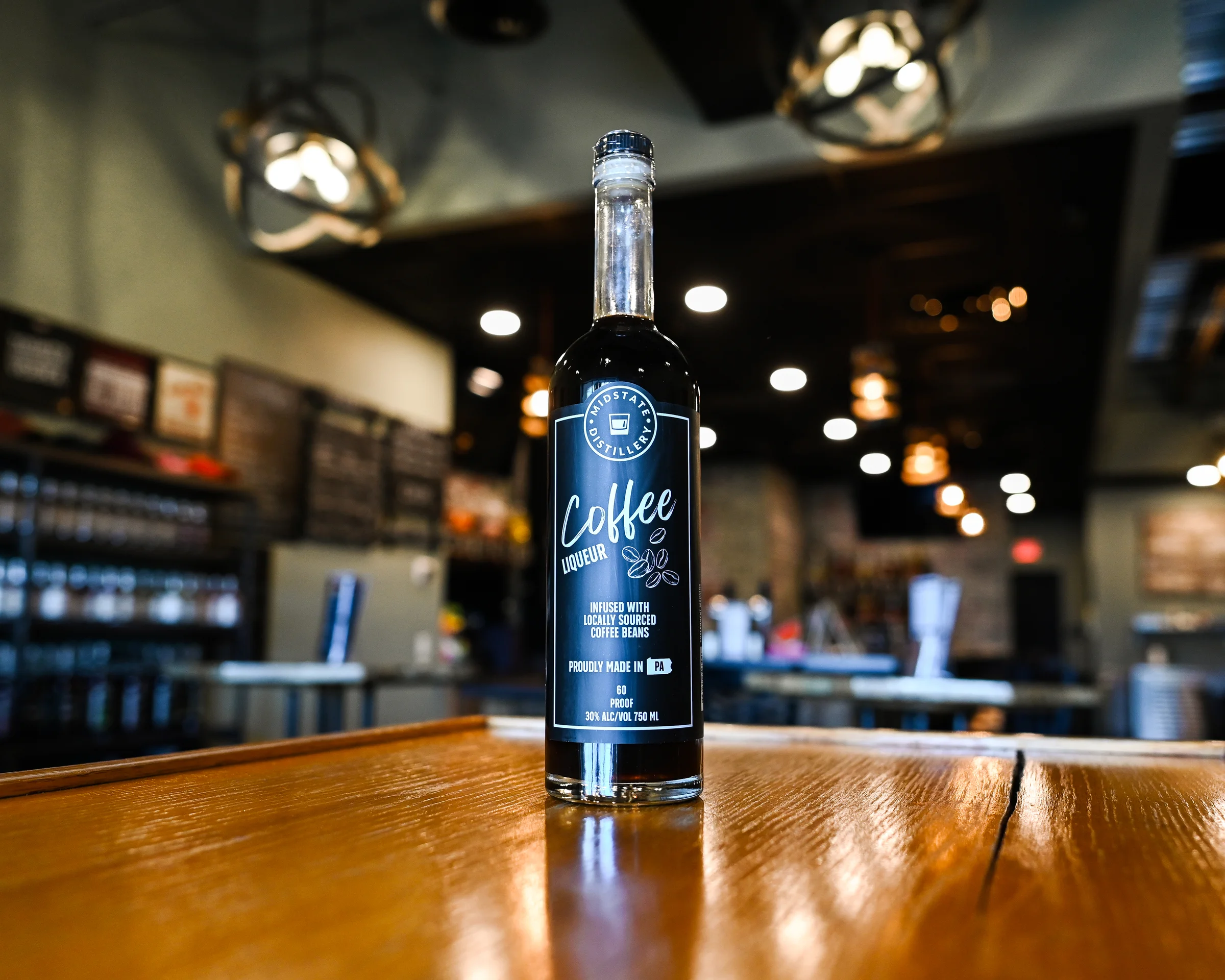 A glass bottle of dark homemade coffee liqueur with a small tumbler beside it on a warm kitchen counter, soft natural light