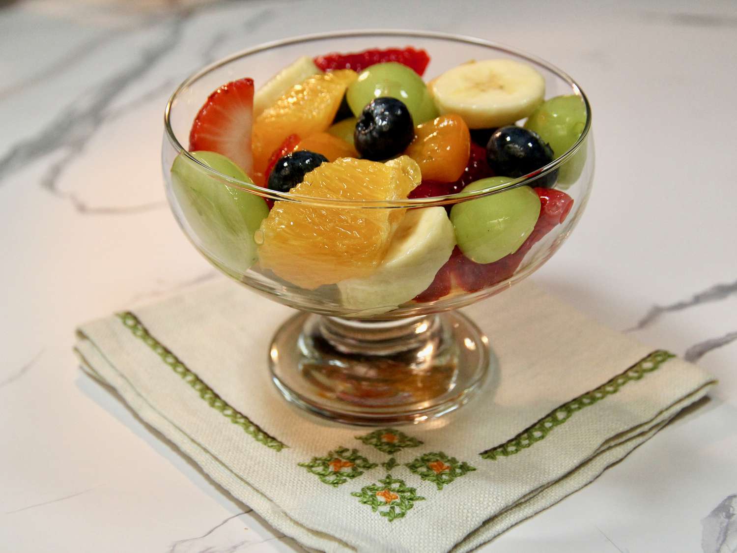 A glass bowl filled with mixed fruit salad including berries, pineapple, and grapes