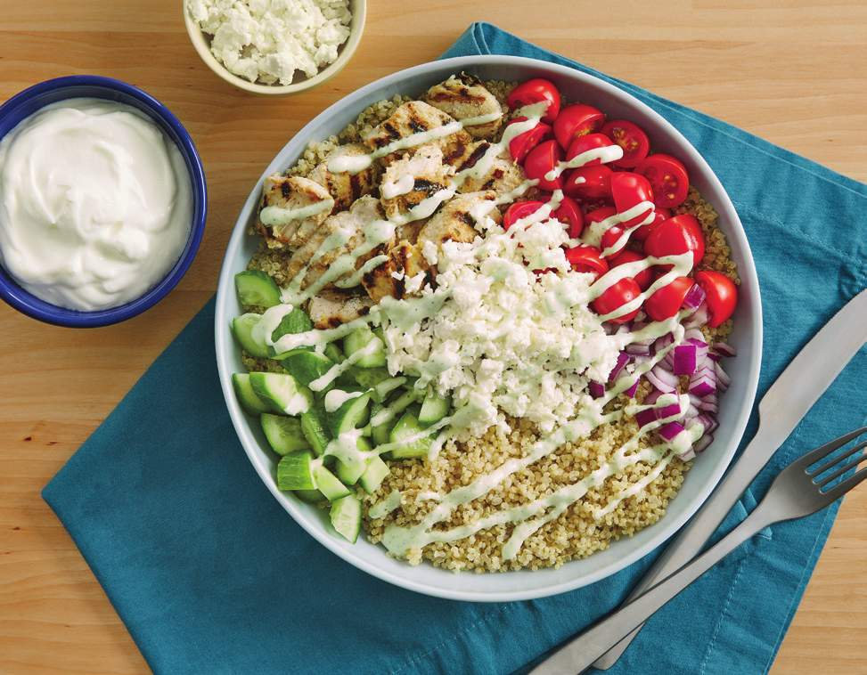 A glass bowl of chicken pieces coated in a pale yogurt and spice marinade on a kitchen counter
