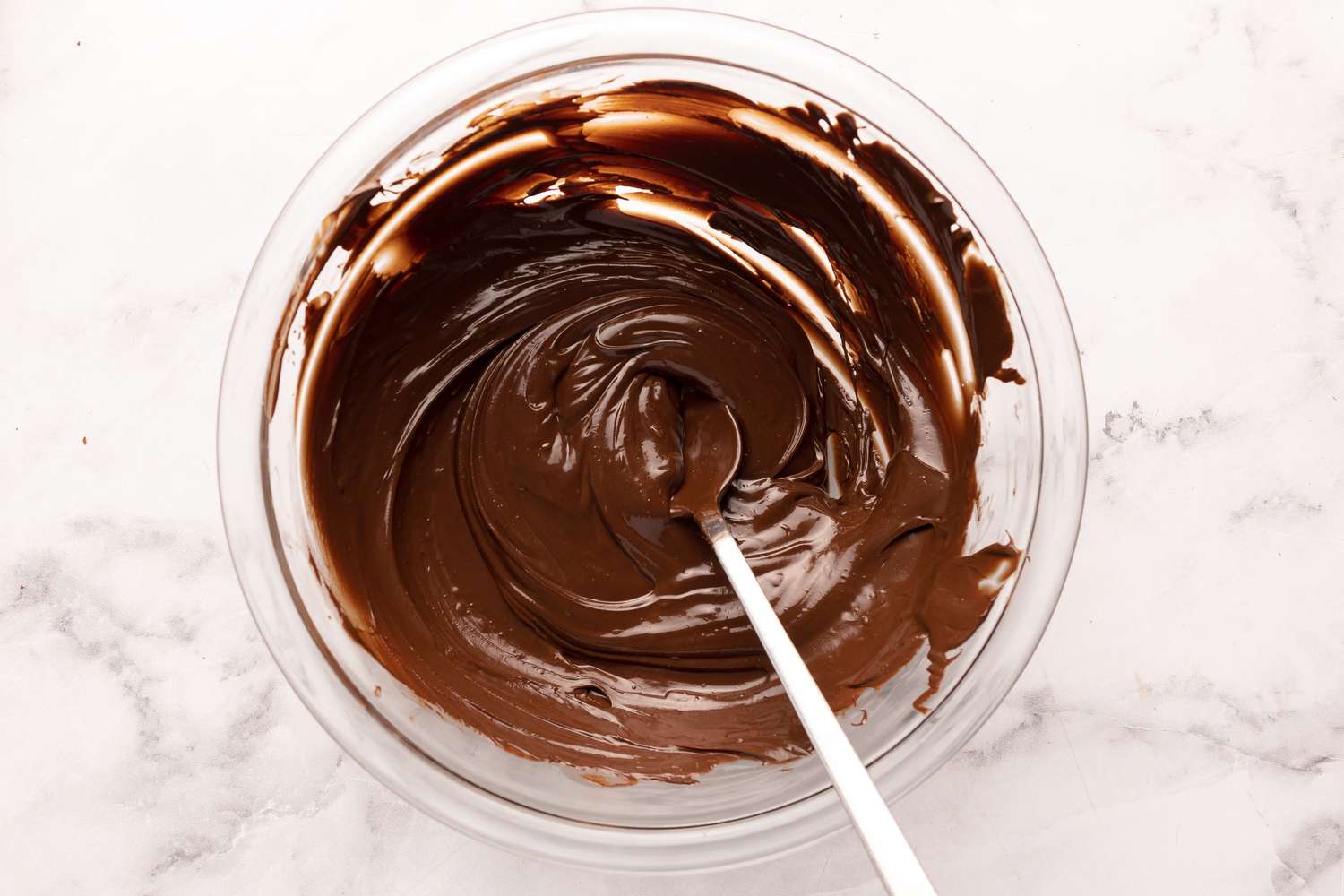 A glass bowl of chocolate chips partially melted and being stirred smooth on a kitchen counter
