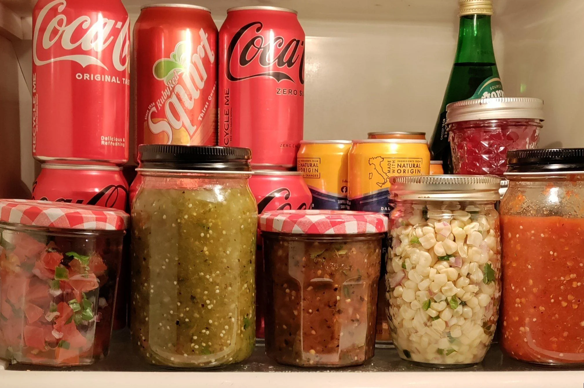 A glass jar filled with green tomatillo salsa on a refrigerator shelf next to a lime and a small container of chopped cilantro
