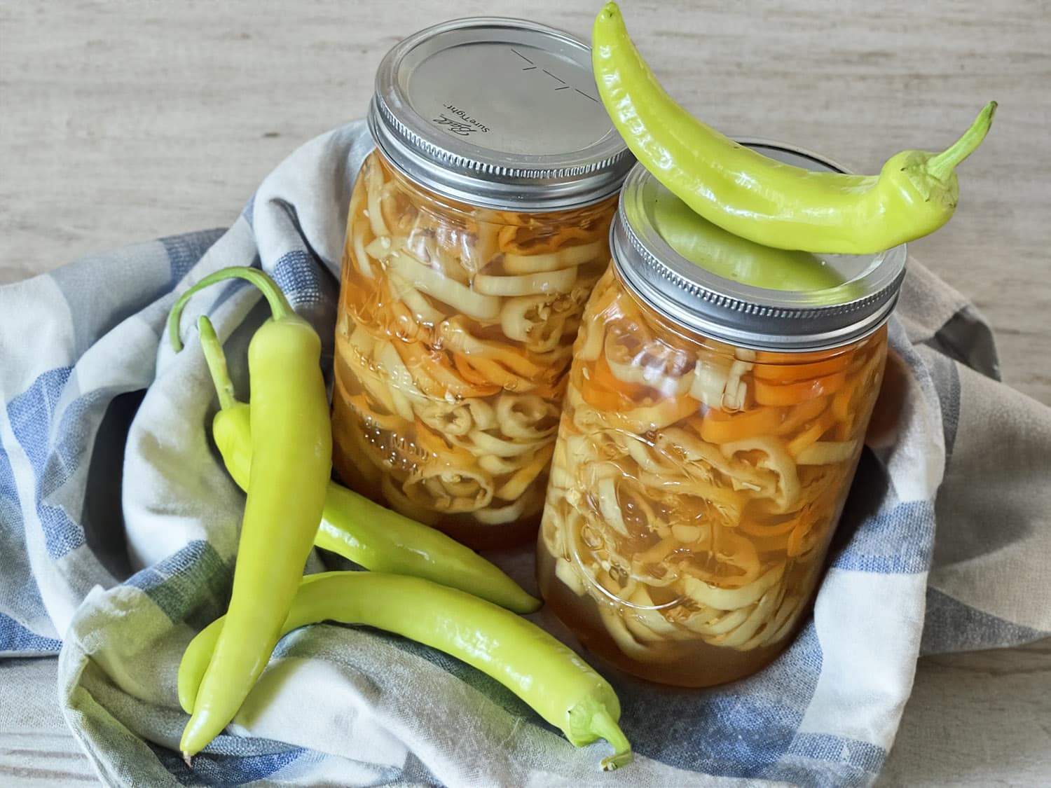 A glass jar filled with quick pickled banana pepper rings in golden brine on a bright kitchen counter with a small bowl of extra pepper rings nearby