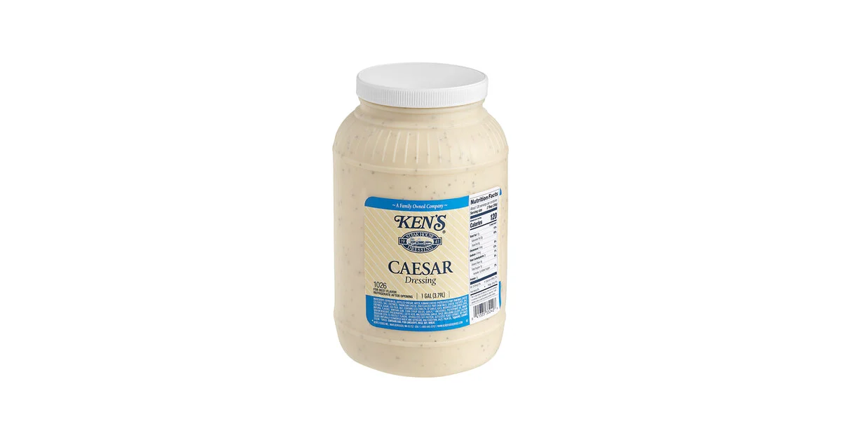 A glass jar of homemade Caesar sauce with a lid on, sitting on a refrigerator shelf next to meal prep containers