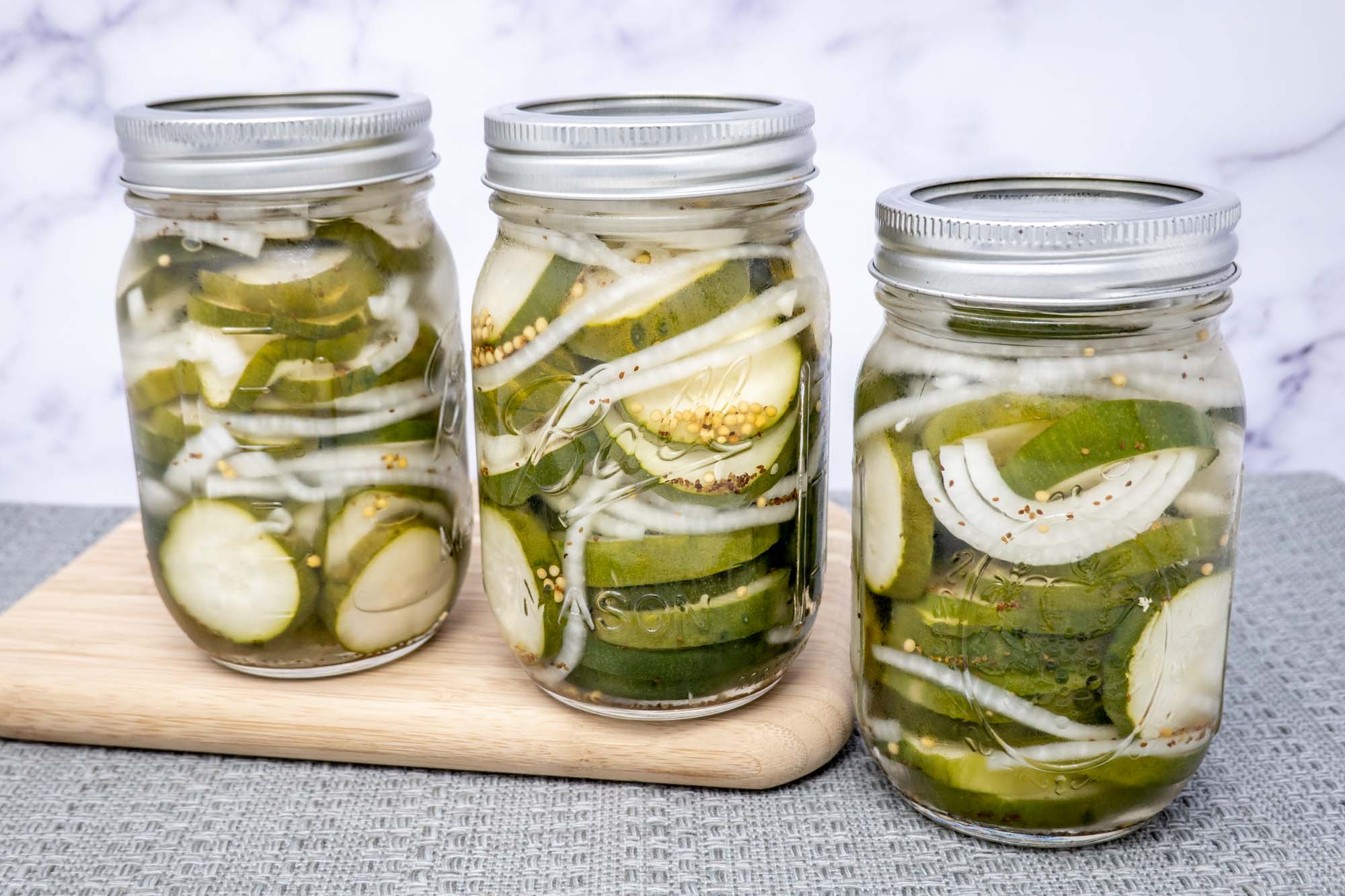 A glass jar of homemade fridge pickles on a bright kitchen counter, with cucumber spears, dill, and garlic visible through the glass