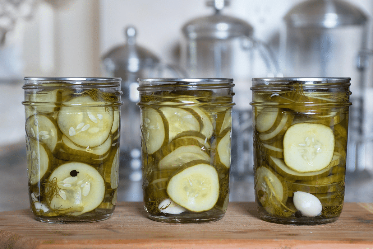 A glass jar of homemade refrigerator dill pickles with garlic cloves and fresh dill on a bright kitchen counter, lid resting nearby