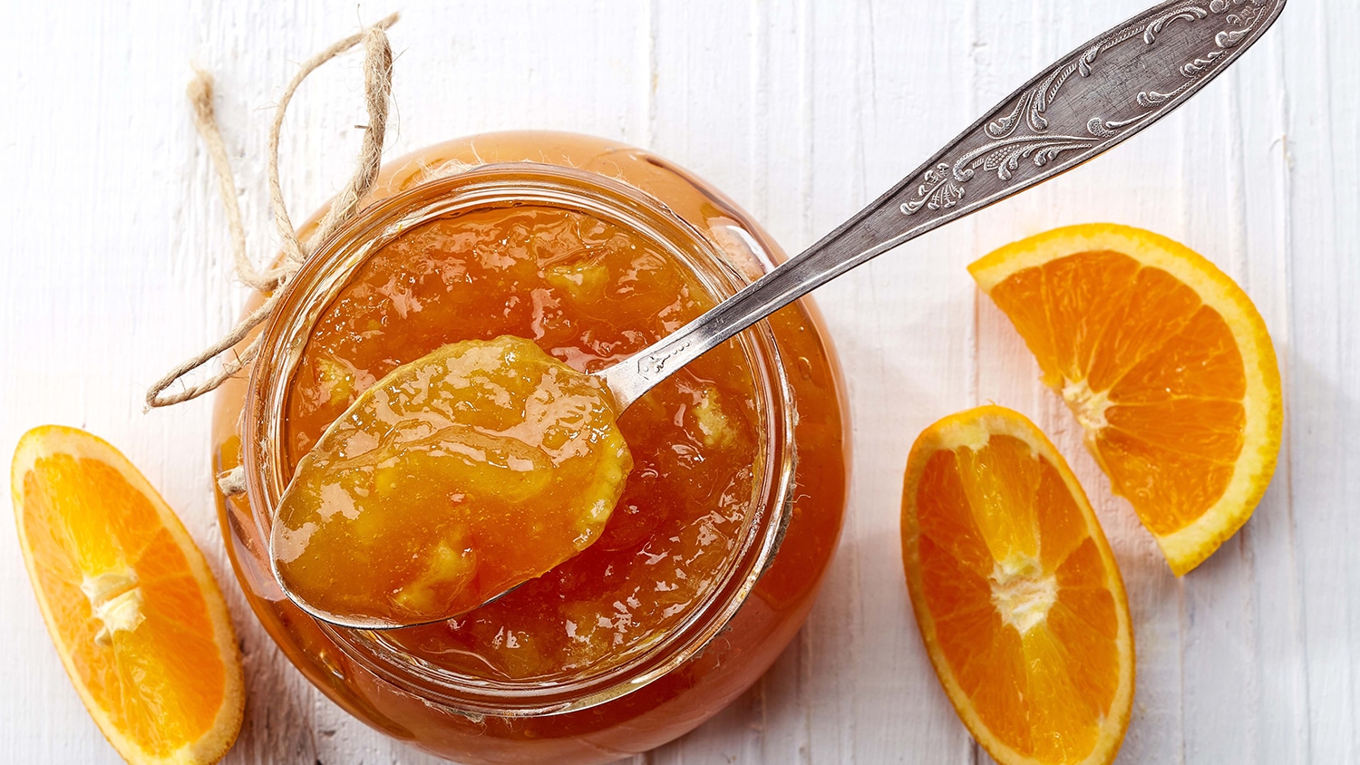 A glass jar of orange marmalade with a spoon resting beside it on a light kitchen counter, morning window light