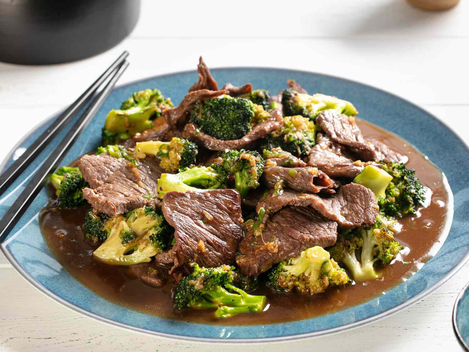 A glass meal prep container filled with beef and broccoli next to a separate container of white rice on a kitchen counter with soft natural lighting