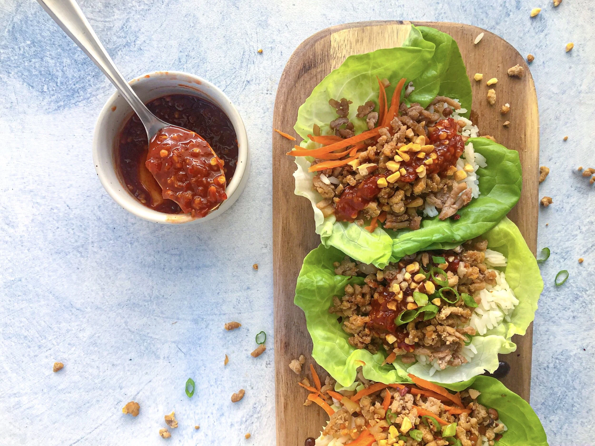 A glass meal prep container filled with cooked lettuce wrap filling next to a separate container of washed butter lettuce leaves on a kitchen counter