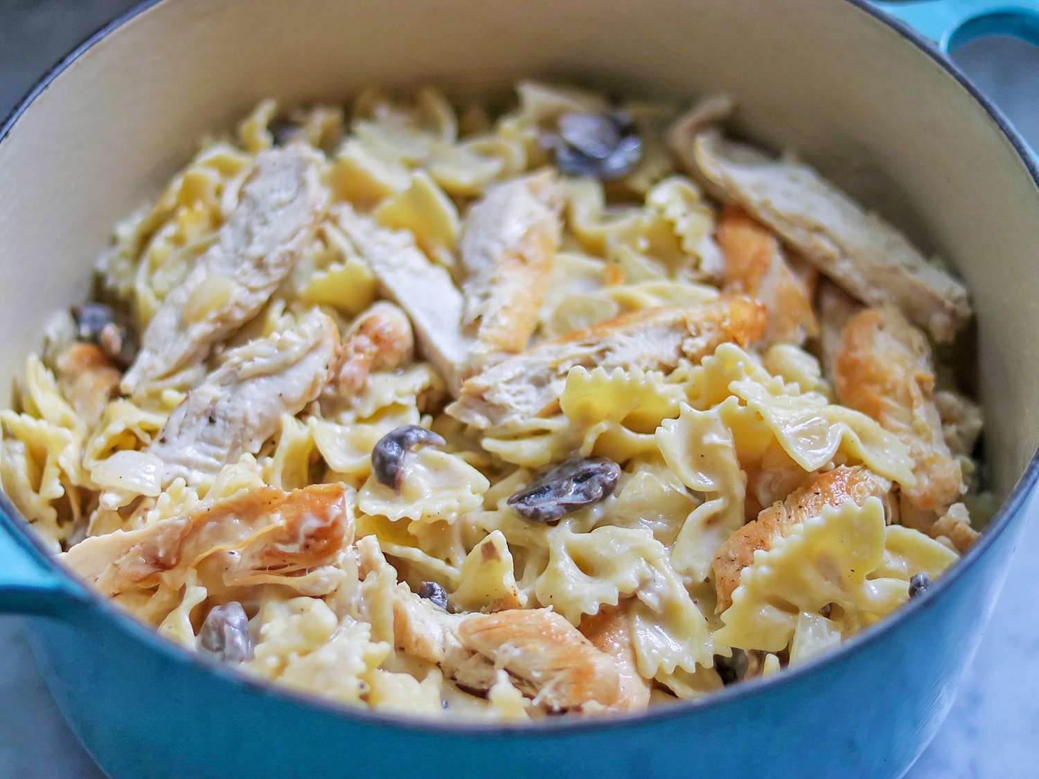 A glass meal prep container filled with creamy chicken pasta and spinach, covered with a lid on a refrigerator shelf