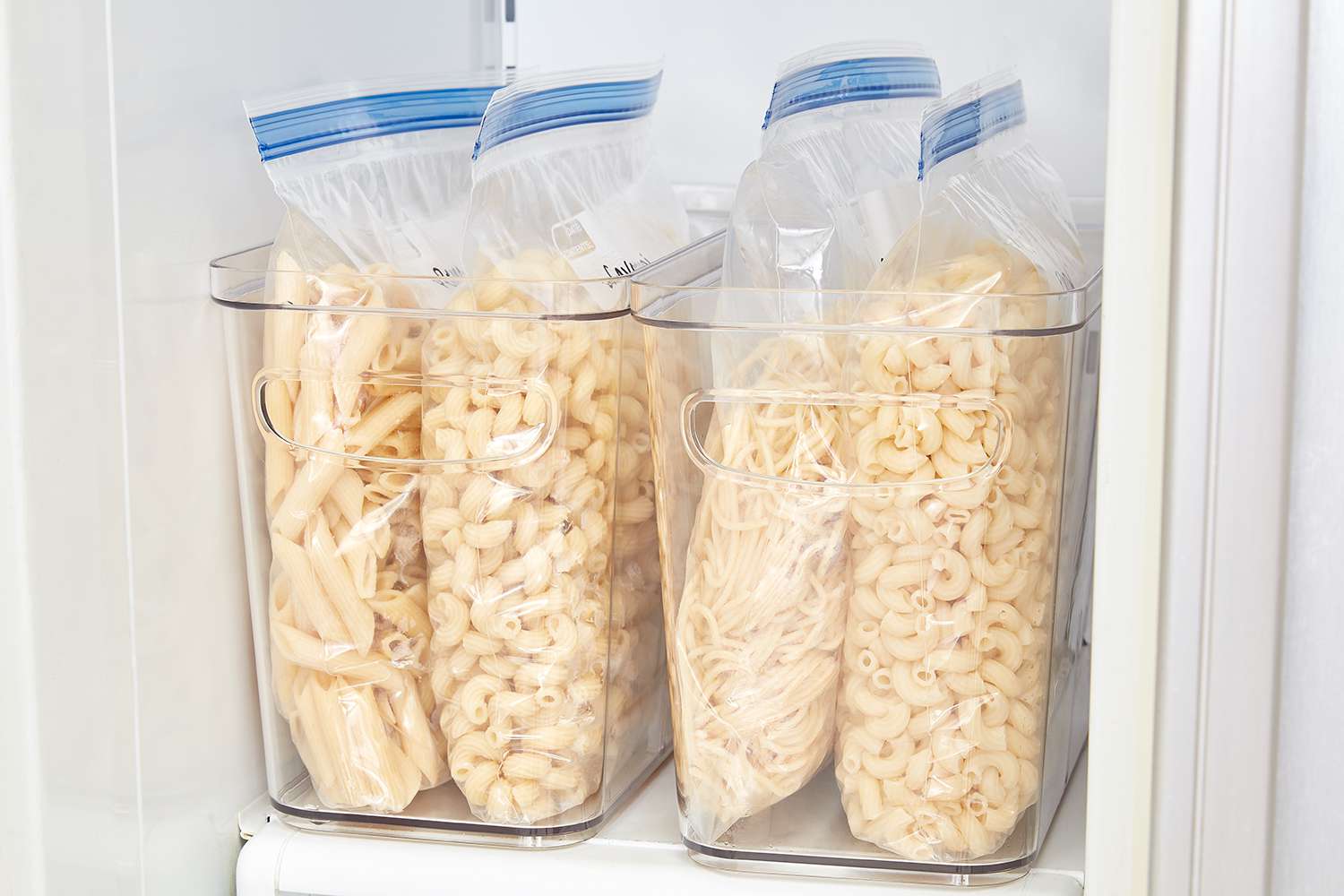 A glass meal prep container filled with creamy sausage pasta on a refrigerator shelf, lid resting beside it